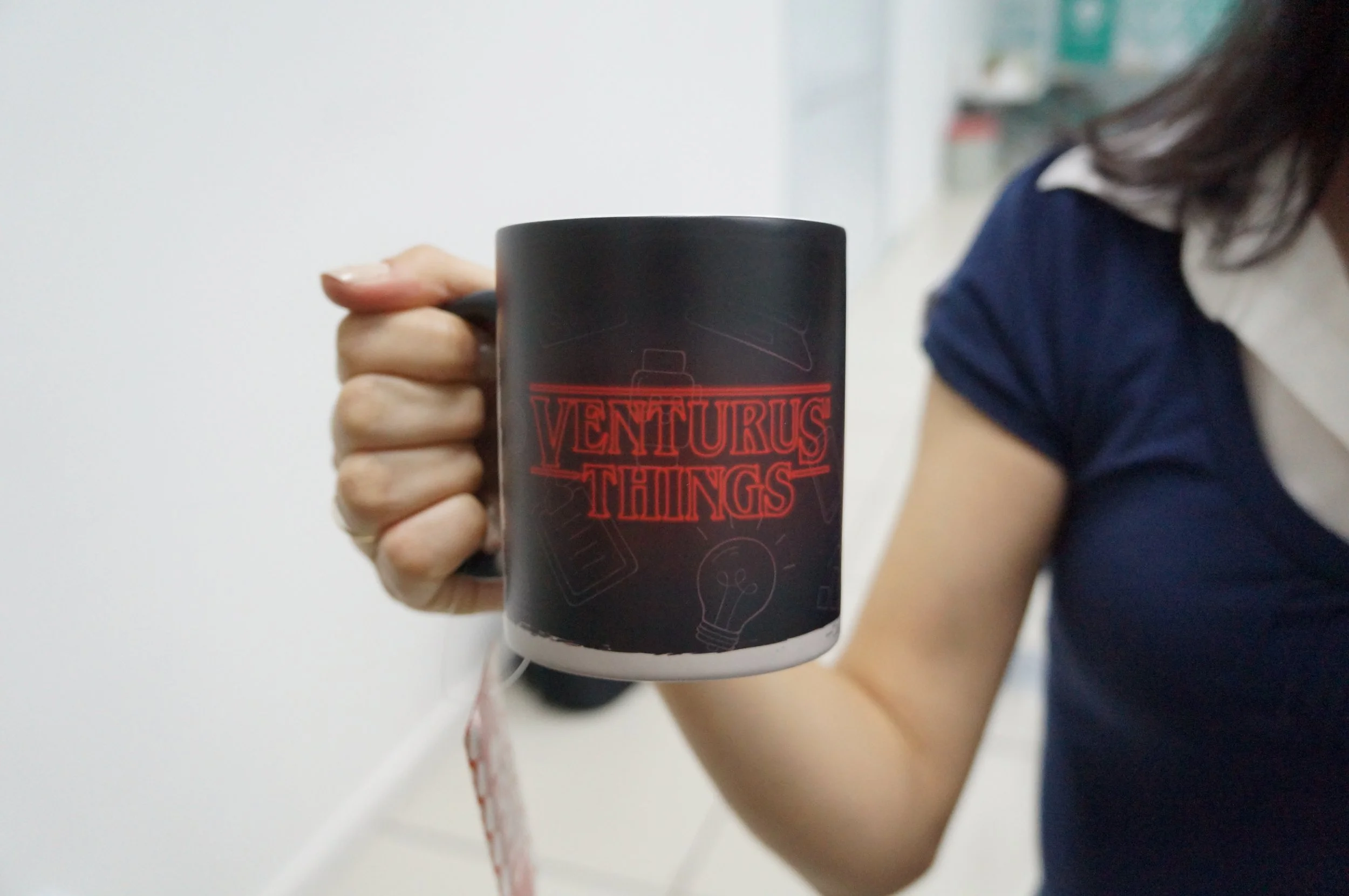 Person holding a black mug with red text that says "VentuRus Things".