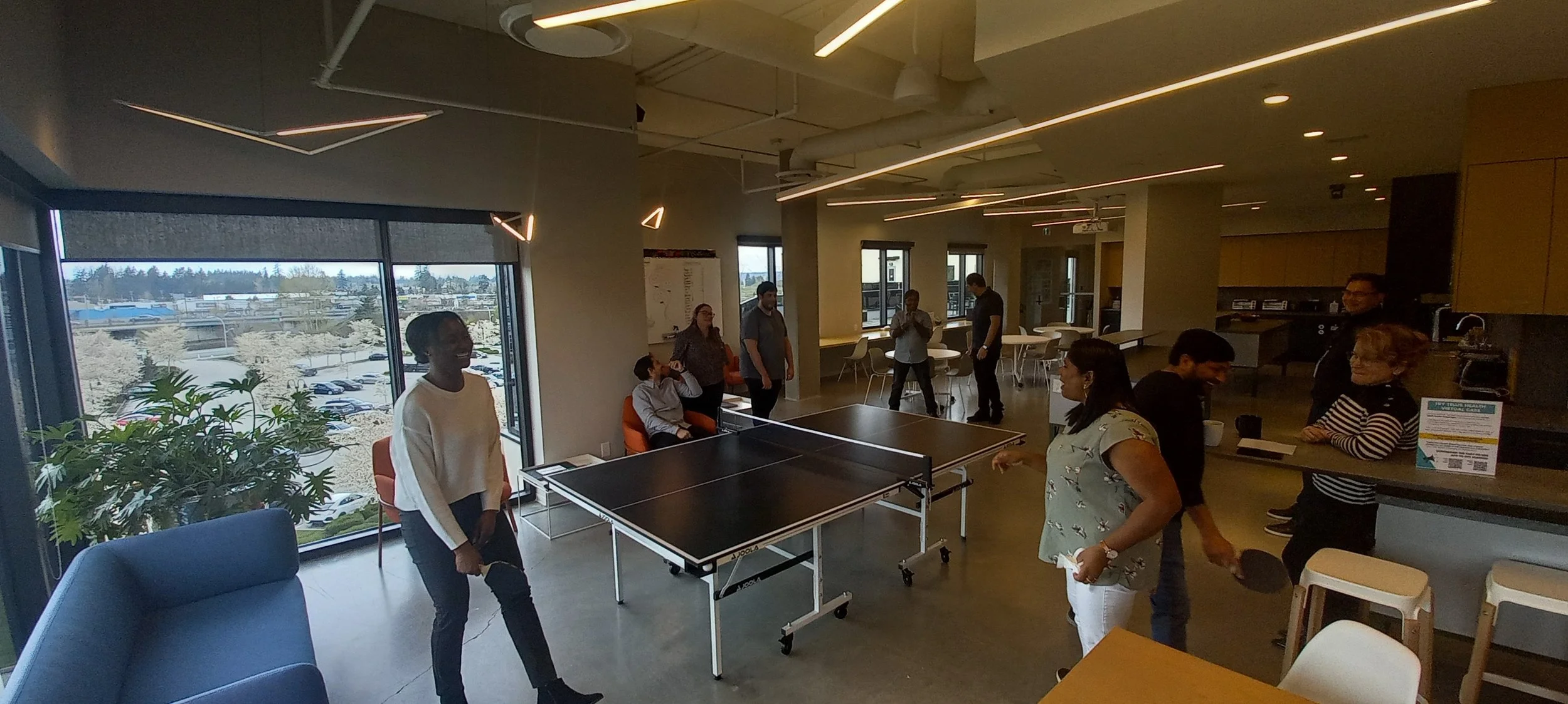 People playing table tennis and socializing in a modern cafe or community space with large windows and stylish lighting.