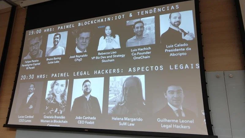 Projection screen displaying two panels of speakers for a conference. The first panel, at 19:00 hours, discusses blockchain, IoT, and trends with five speakers whose photos and names are shown. The second panel, at 20:30 hours, covers legal aspects o