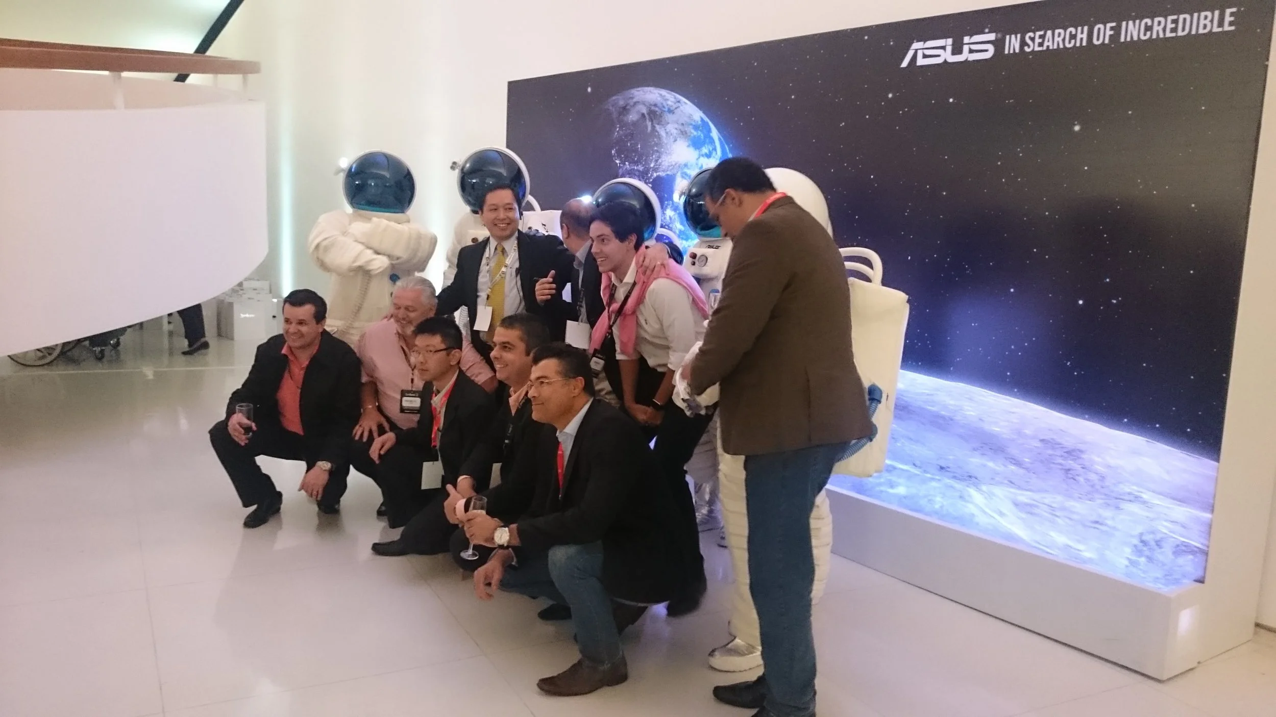 Group of people in front of an ASUS backdrop with space and earth showing, some wearing astronaut helmets, posing for a photo at an event.