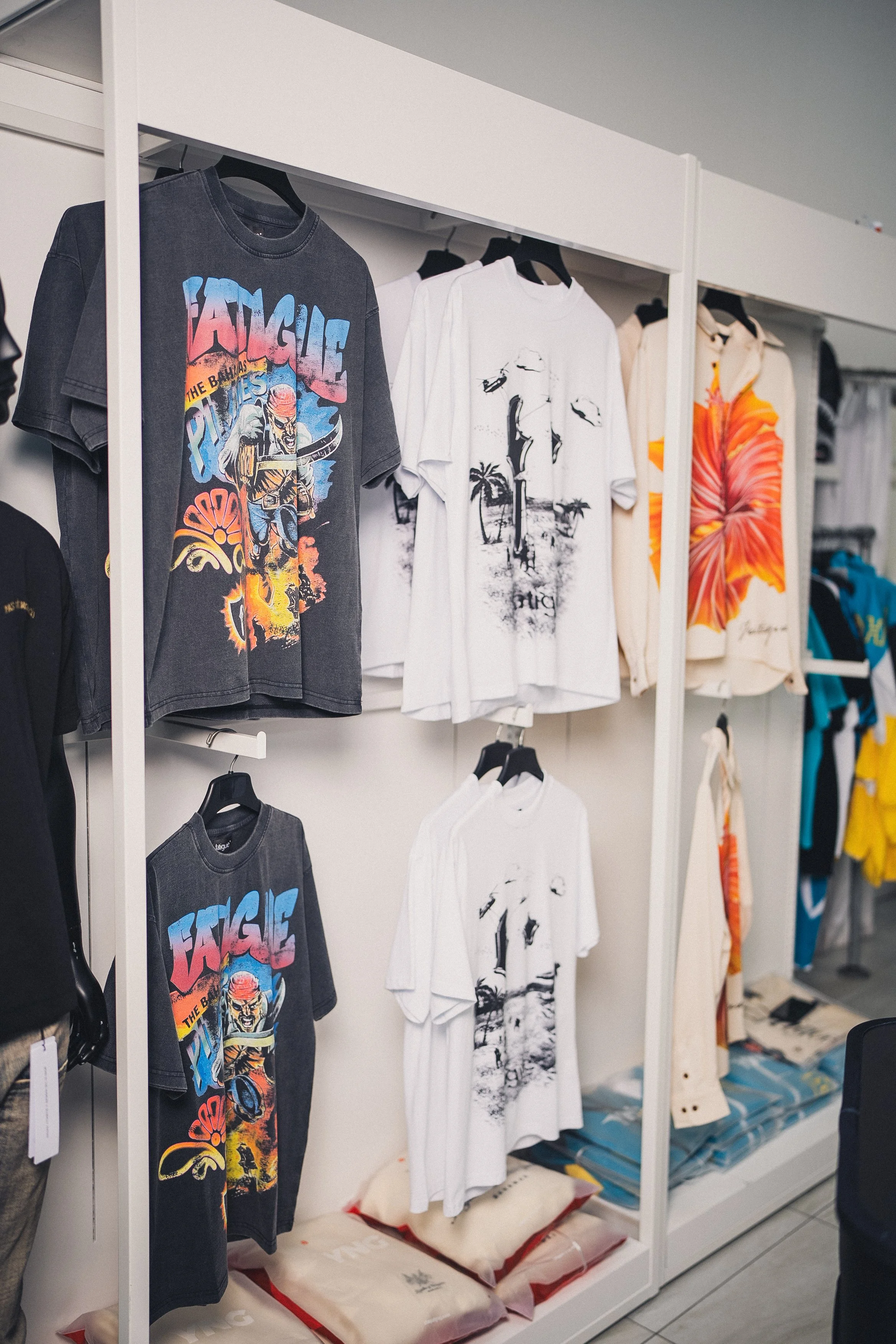 Display of graphic T-shirts with colorful and black-and-white designs hanging on racks in a store.