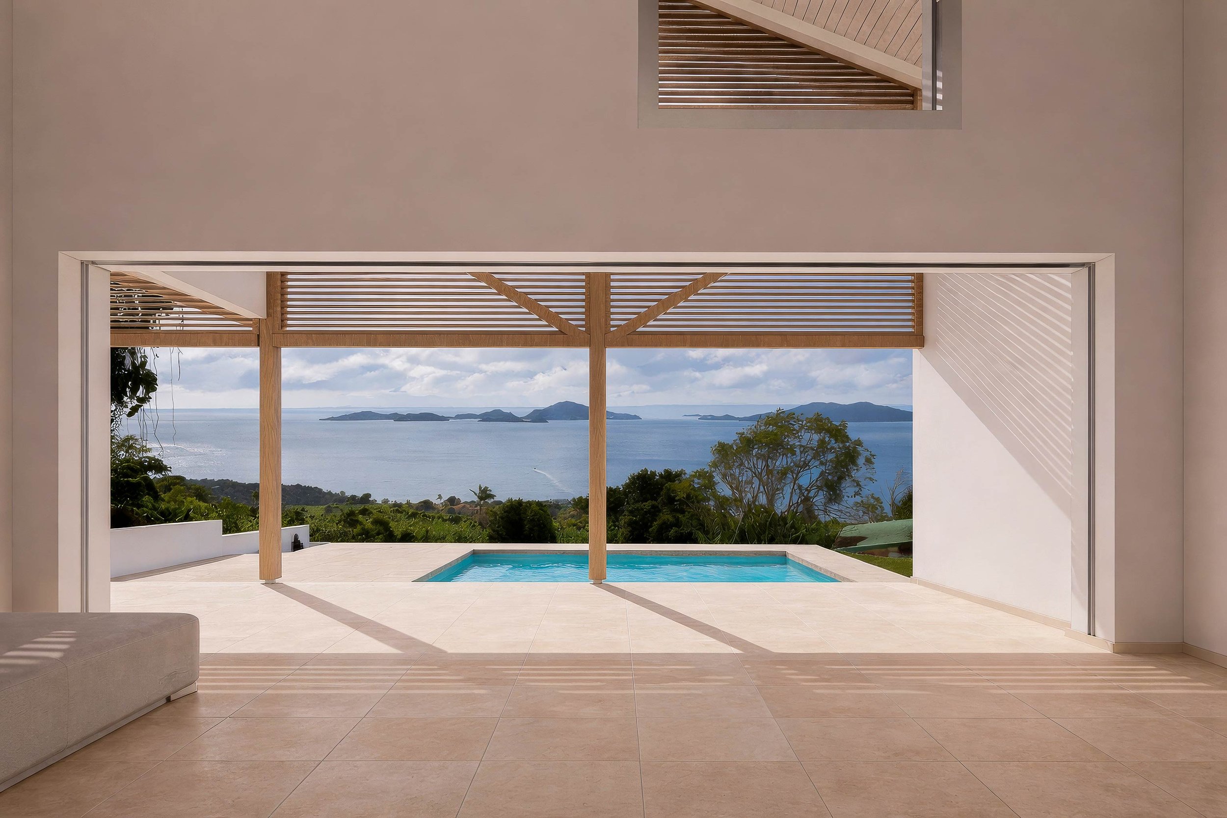 Cadrage depuis le séjour vers la piscine et la mer des Caraïbes. Vue panoramique sur Les Saintes. Structure bois en V et pergola à lames horizontales.