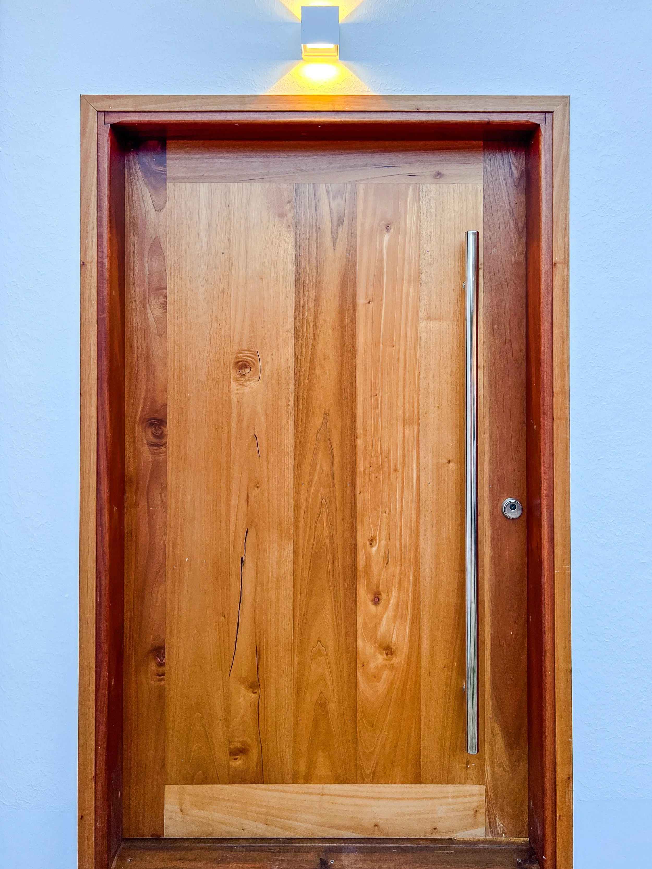 Porte en bois avec poignée longue, encadrée en bois, éclairée par une lumière décorative