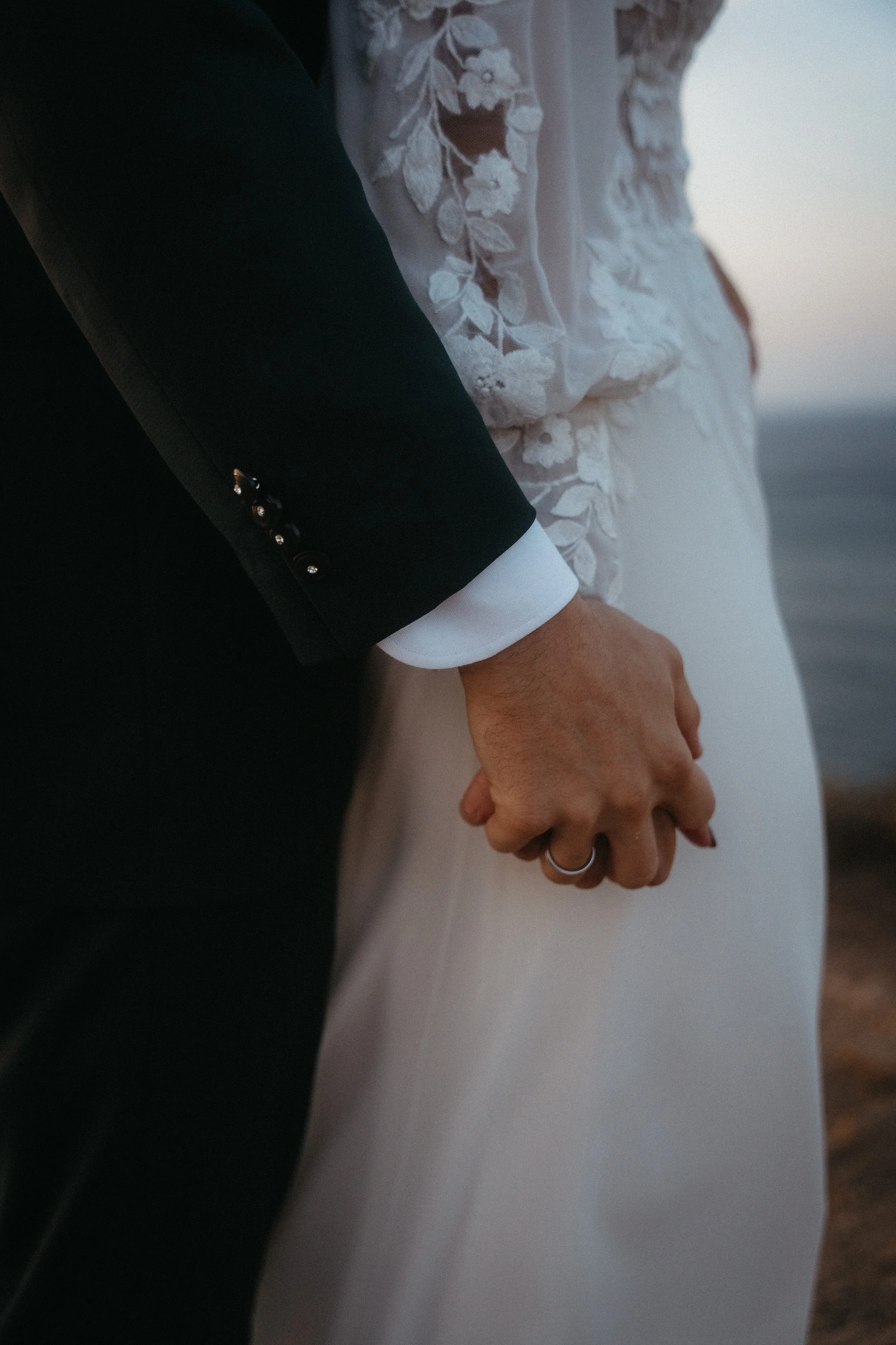 Persona con traje formal y vestido de novia sosteniendo de la mano en un escenario al aire libre.