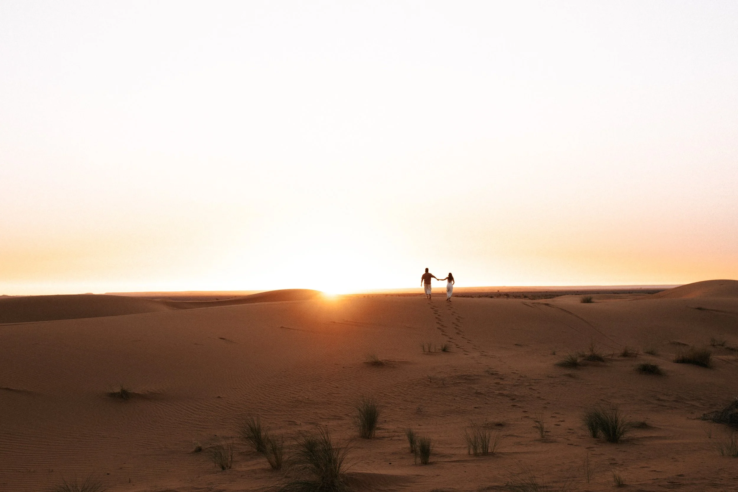 Pareja caminando en las dunas del desierto al atardecer.