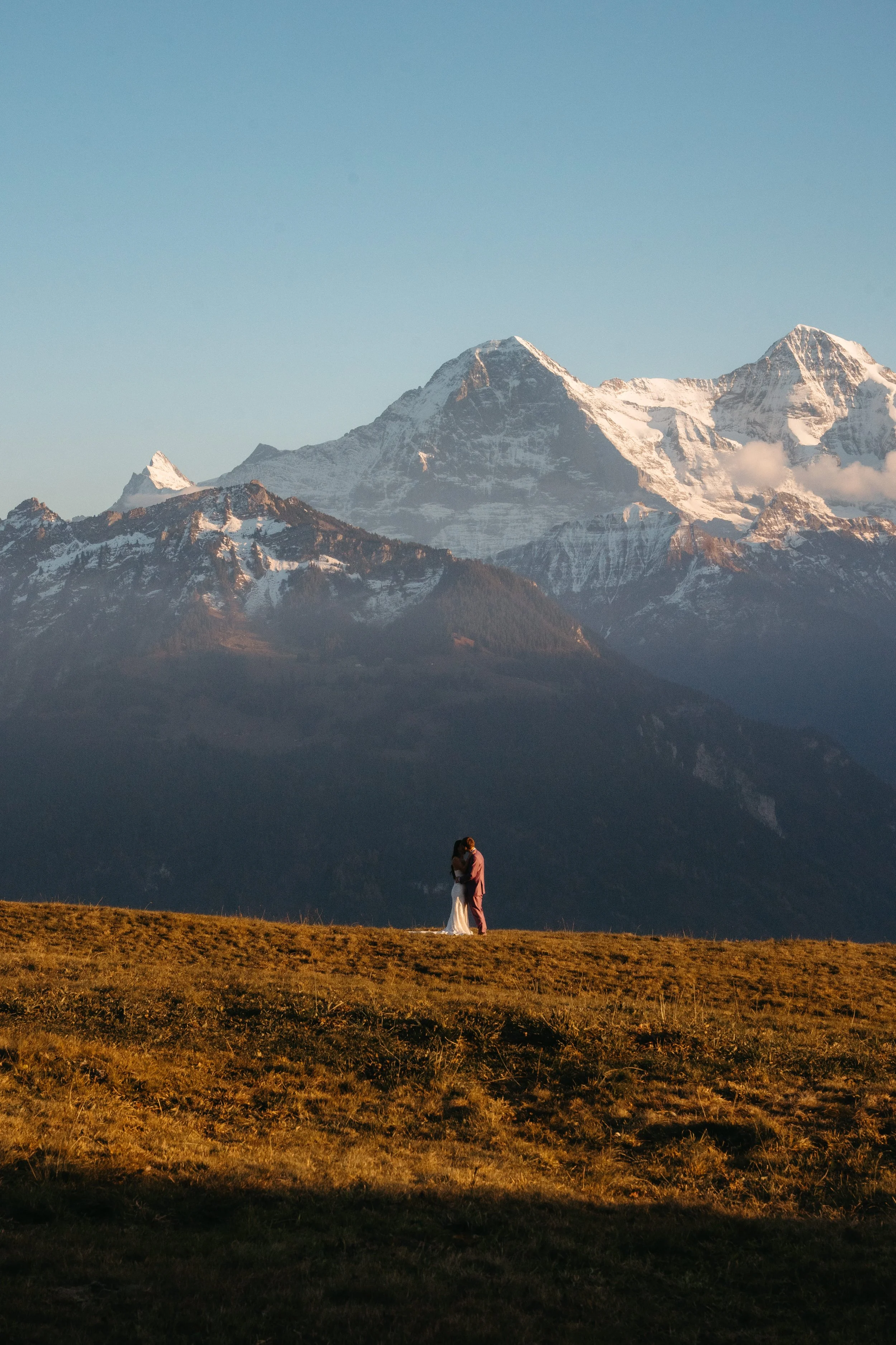 Una pareja de novios abrazados en un campo con montañas nevadas al fondo