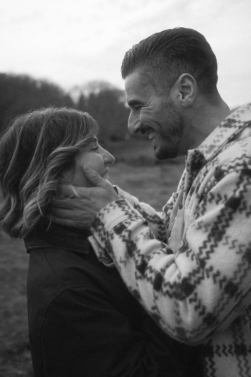 Una pareja sonriente en un campo, el hombre sostiene la cara de la mujer con una mano, en una fotografía en blanco y negro.