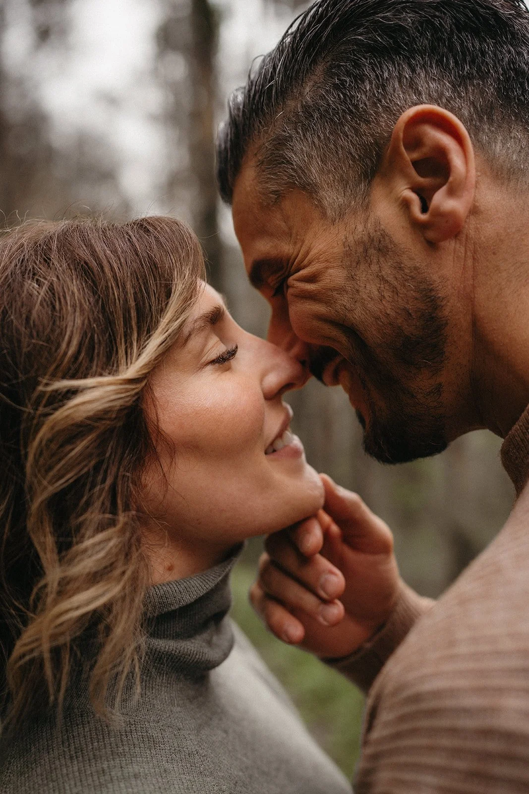 Una pareja se está tocando la frente y sonriendo con los ojos cerrados en un entorno natural.