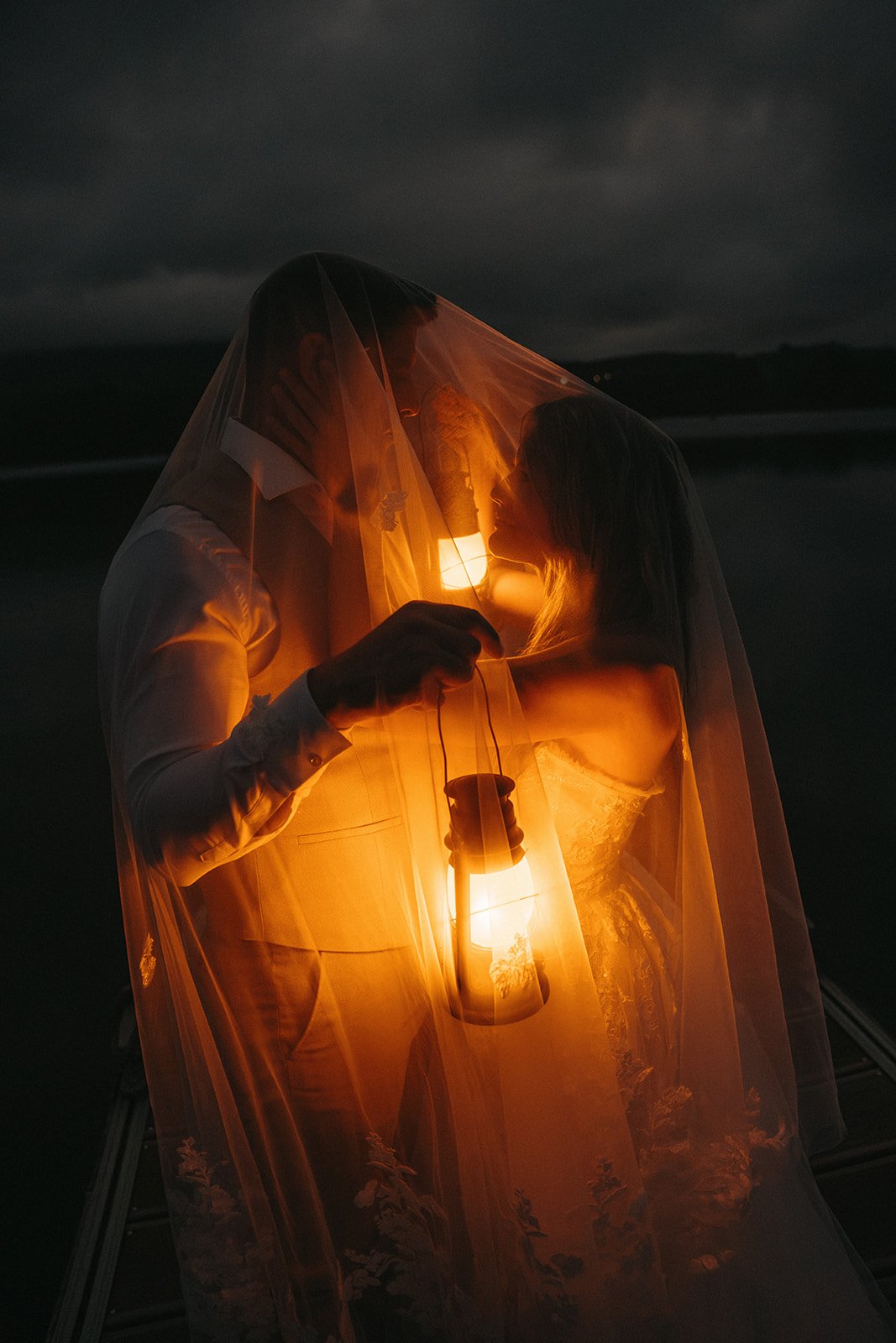 Una pareja en un momento romántico en la playa, envuelta por una cortina de tela transparente y sosteniendo una linterna en la noche.