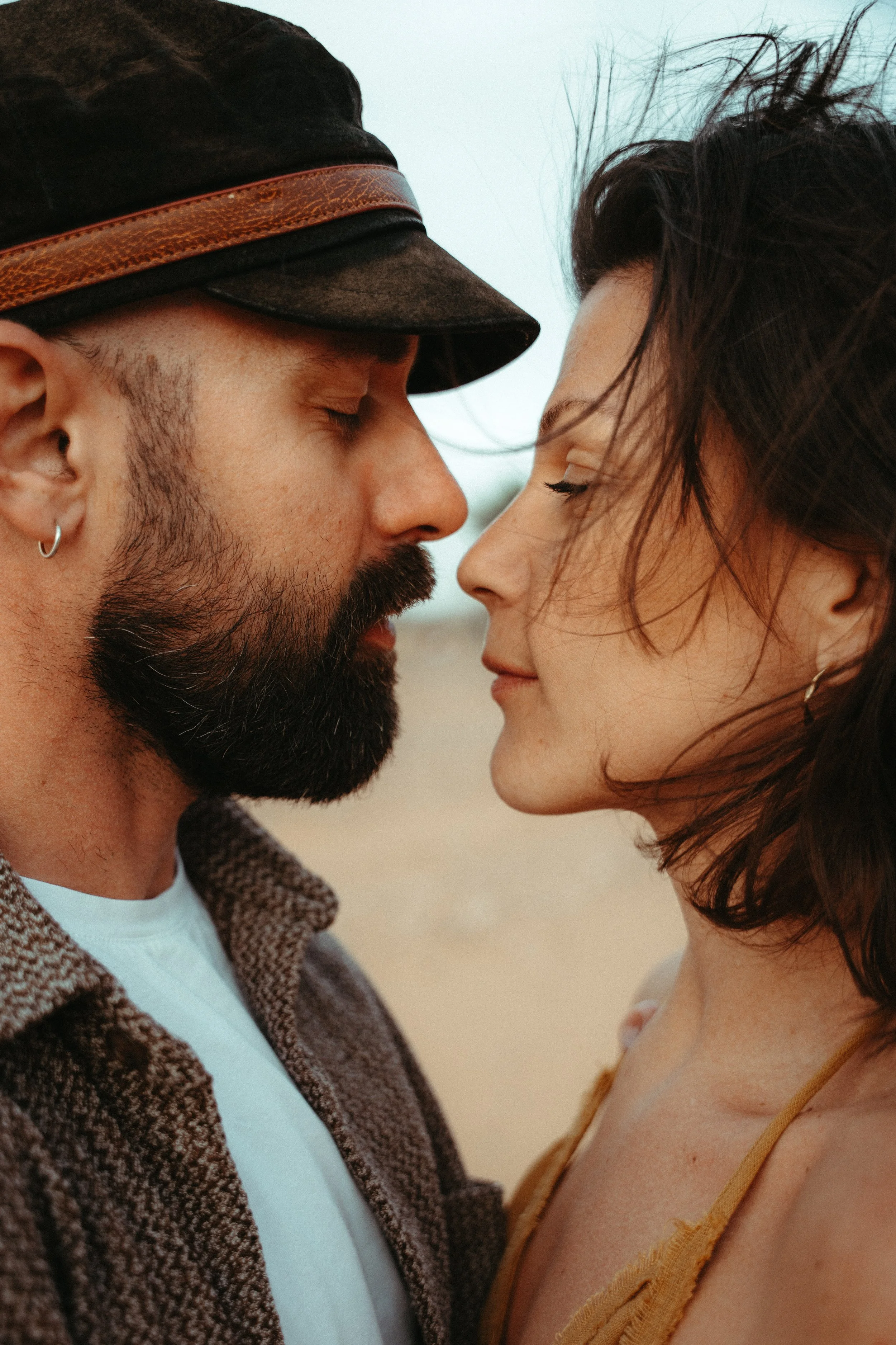 Una pareja se acerca y se observa en un fondo de arena y cielo nublado.
