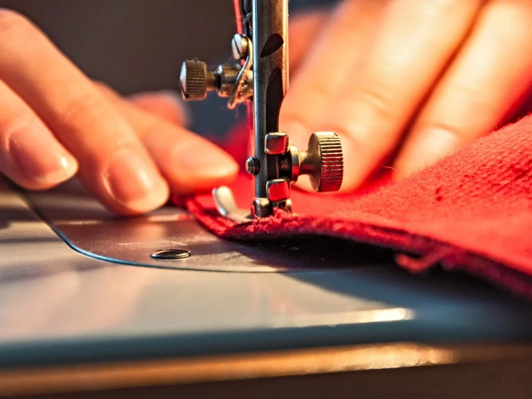 Close-up of a sewing machine stitching red fabric, with hands guiding the fabric through the machine.