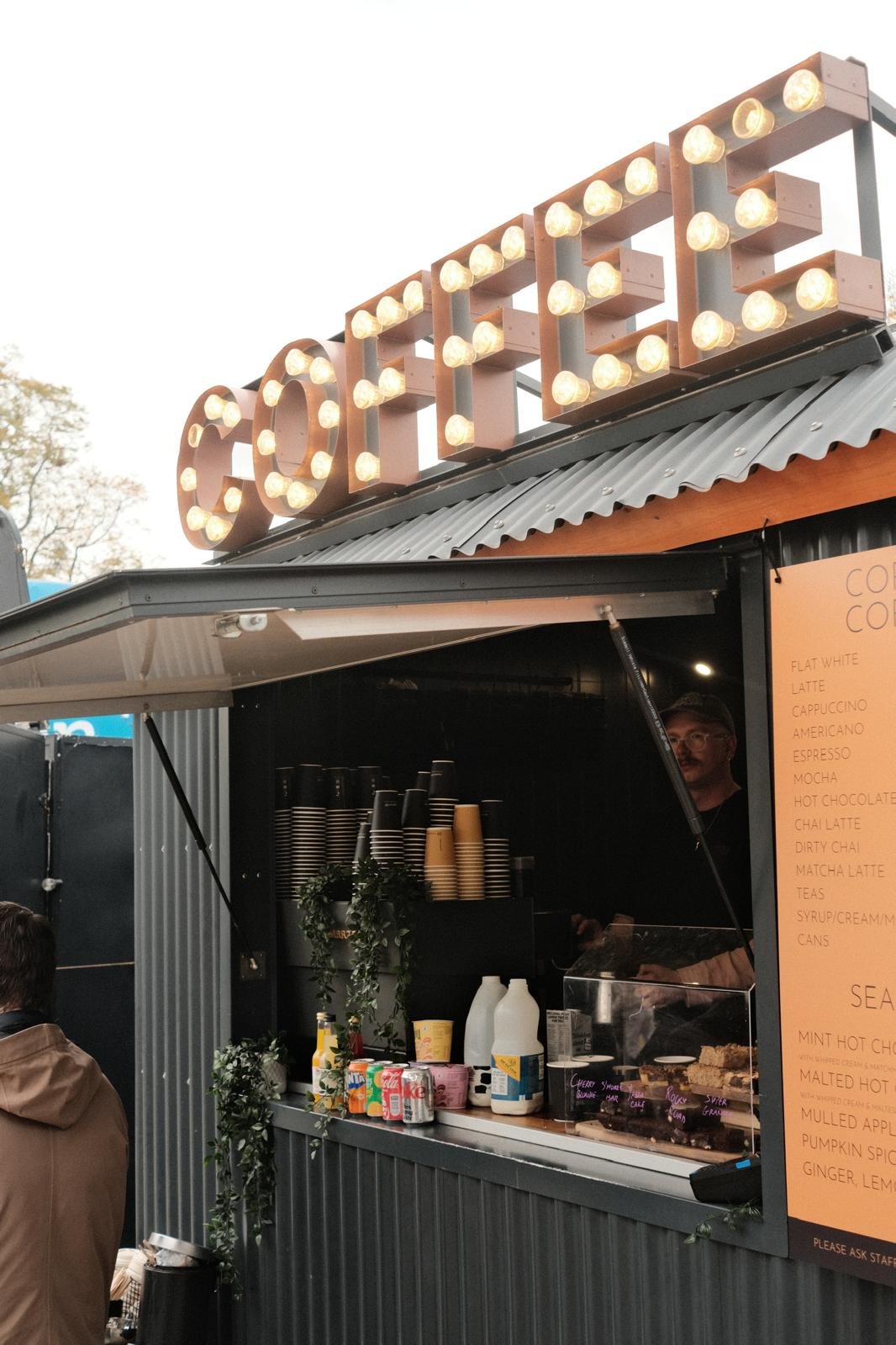 anthracite grey shepherds hut with coffee machine, cake display & light up lettering on the roof reads coffee