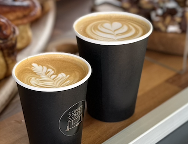 two barista made flat whites with latte art served in takeaway cups at an outdoor event