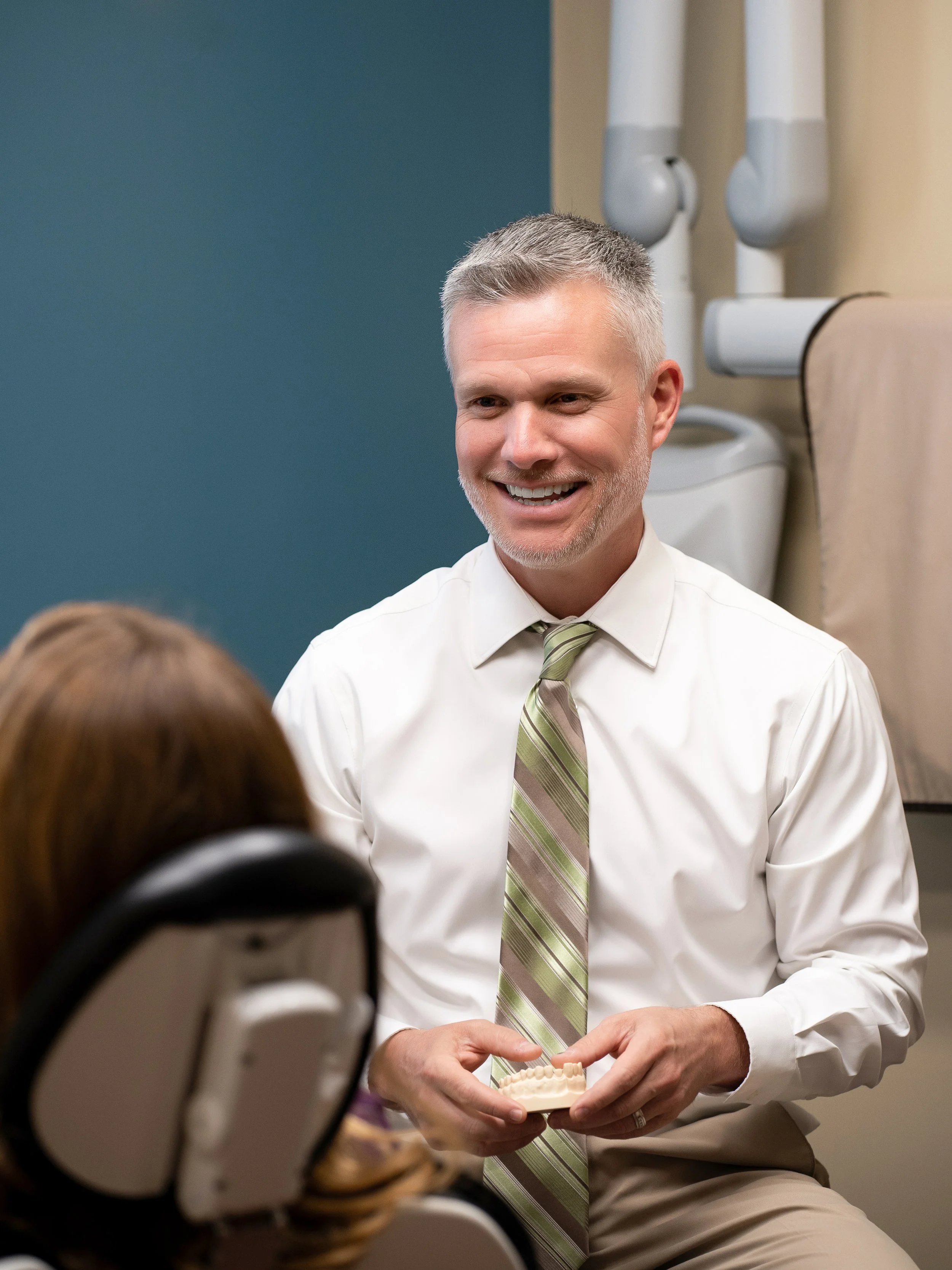 Dr. Shephard smiling and conversing with a patient seated in a dental chair in a treatment room.