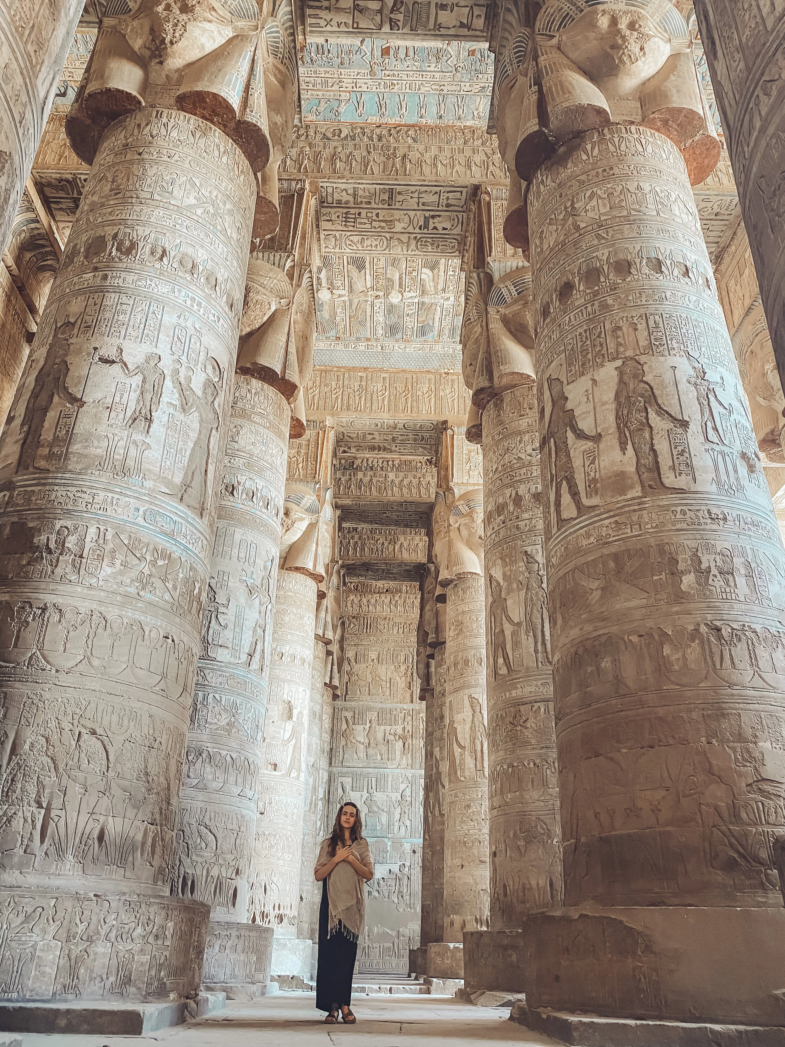A woman standing inside an ancient Egyptian temple with large stone columns covered in hieroglyphics and carvings.