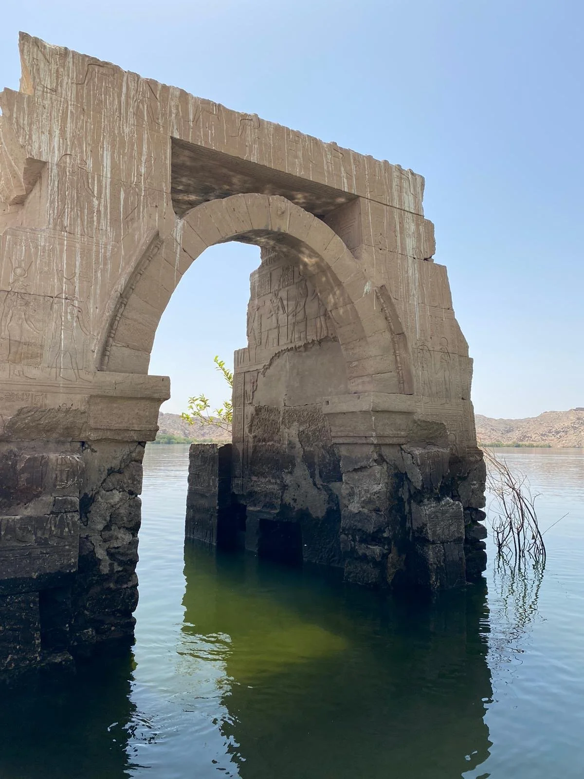 Ancient stone archway ruins partially submerged in water with distant hills in the background.