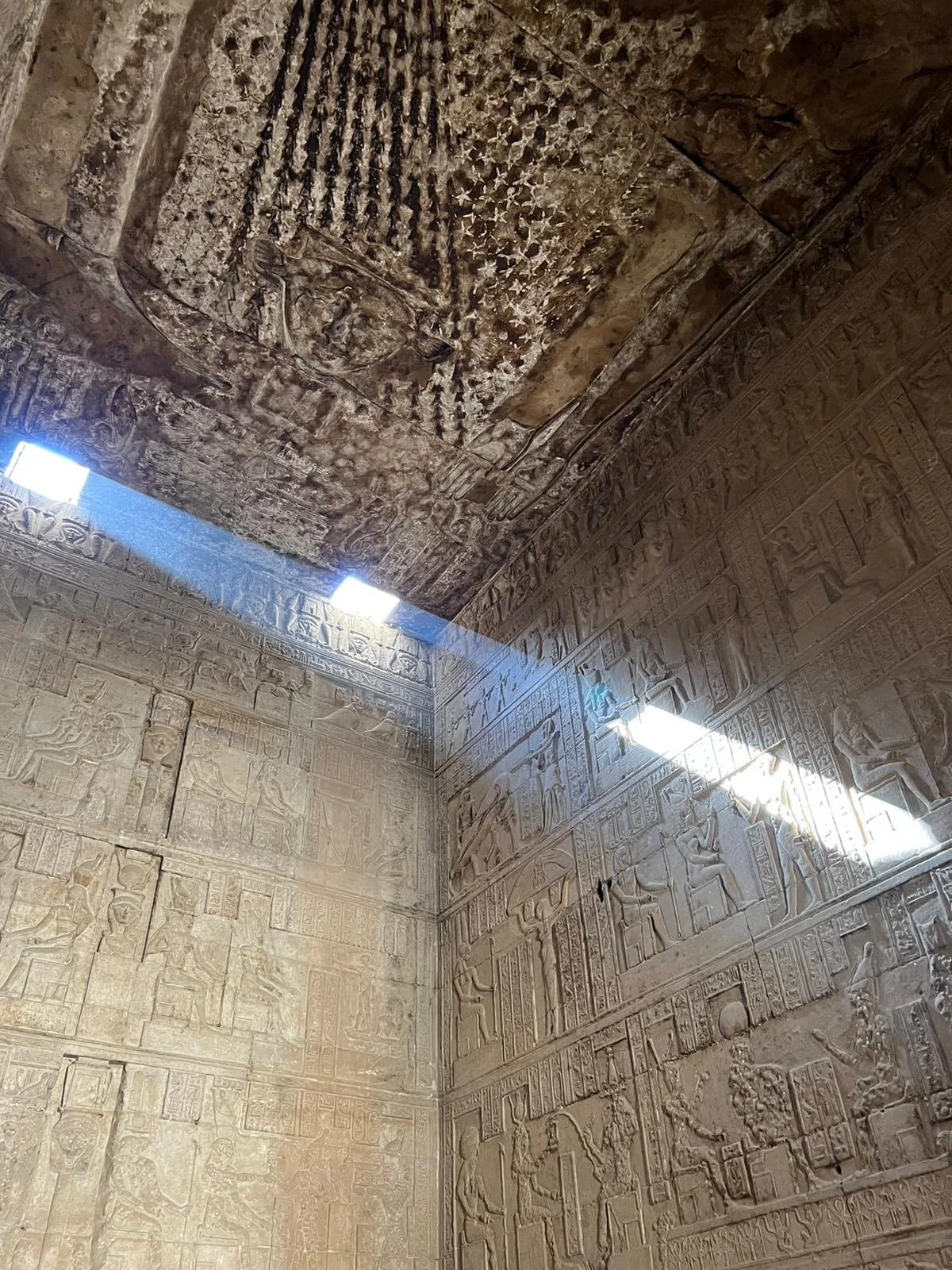 Interior of an ancient Egyptian tomb showing hieroglyphic carvings and a ceiling with a large carved pattern.