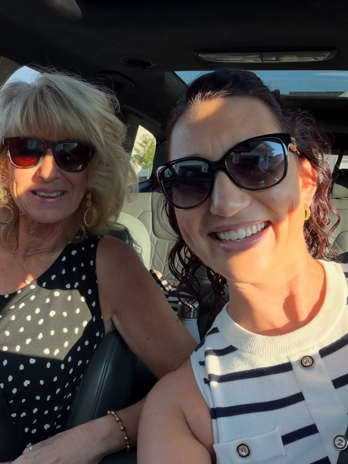 Two women taking a selfie inside a car, wearing sunglasses and smiling.
