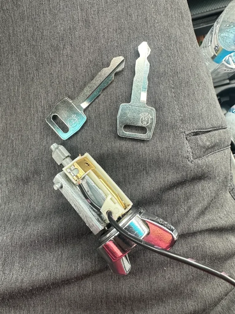 Examining a car key fob with parts and key blades on gray fabric.