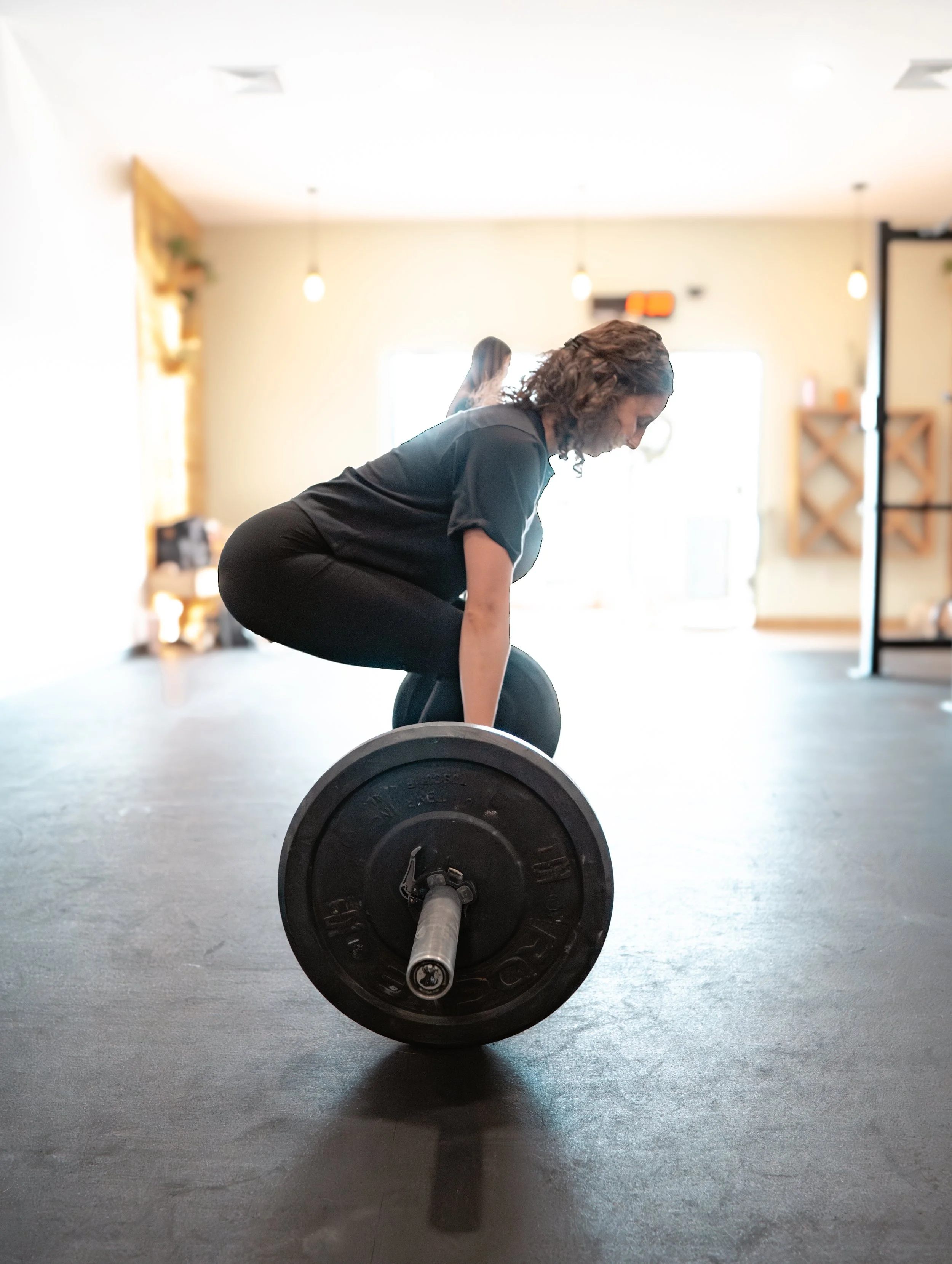 Woman in black workout clothes lifting a barbell in a gym.