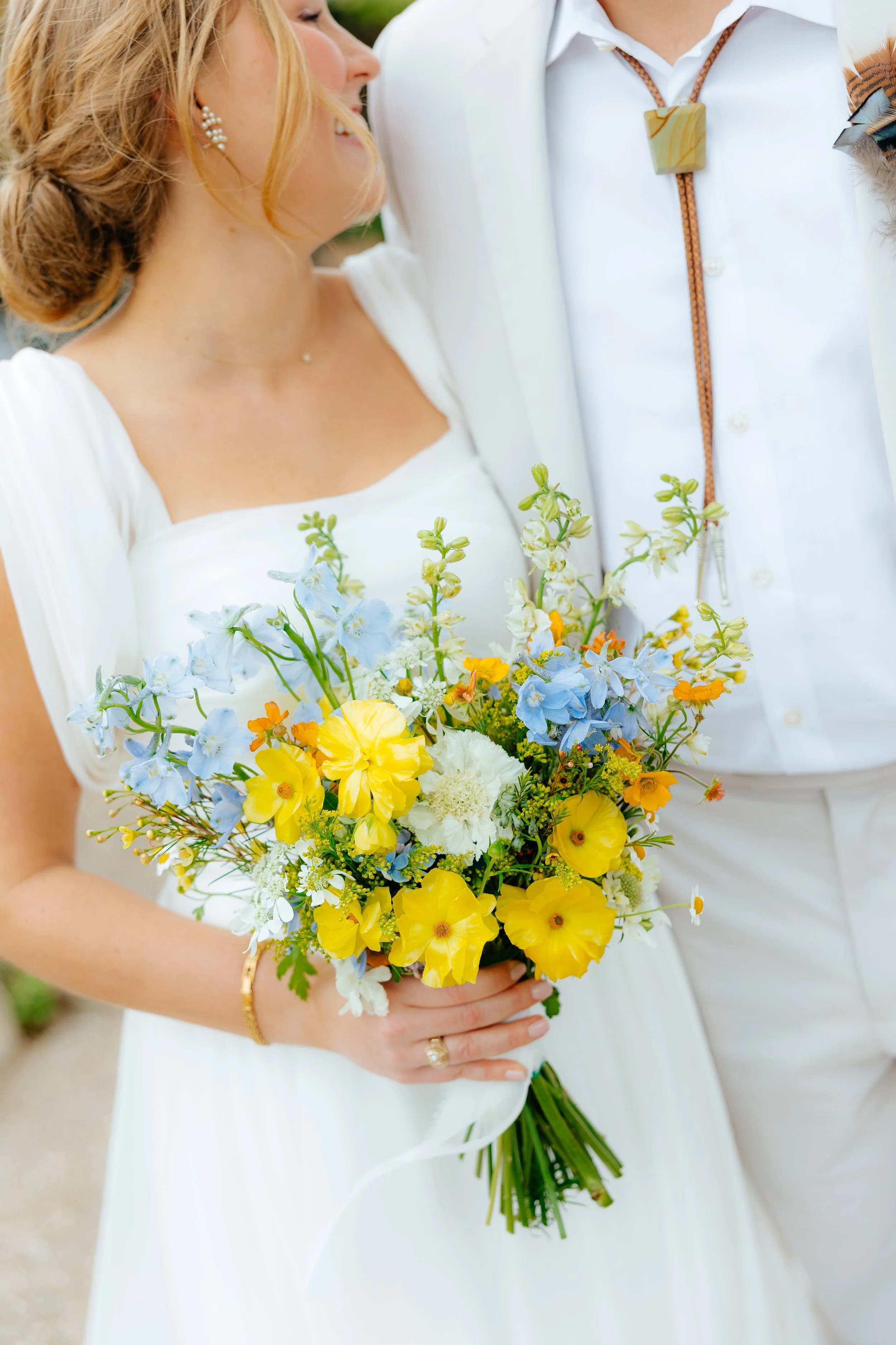 Bride holding a colorful bouquet of yellow, white, and blue flowers during a wedding.