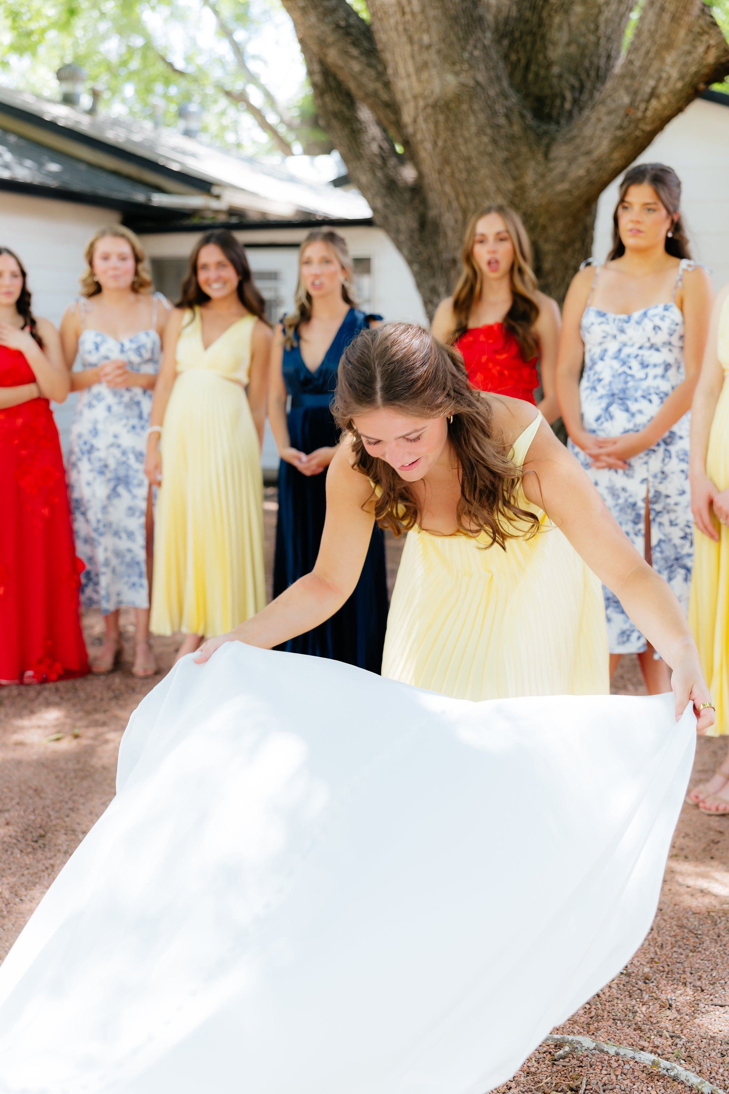 A woman in a yellow dress is preparing her wedding dress for the ceremony while other women in colorful dresses observe.