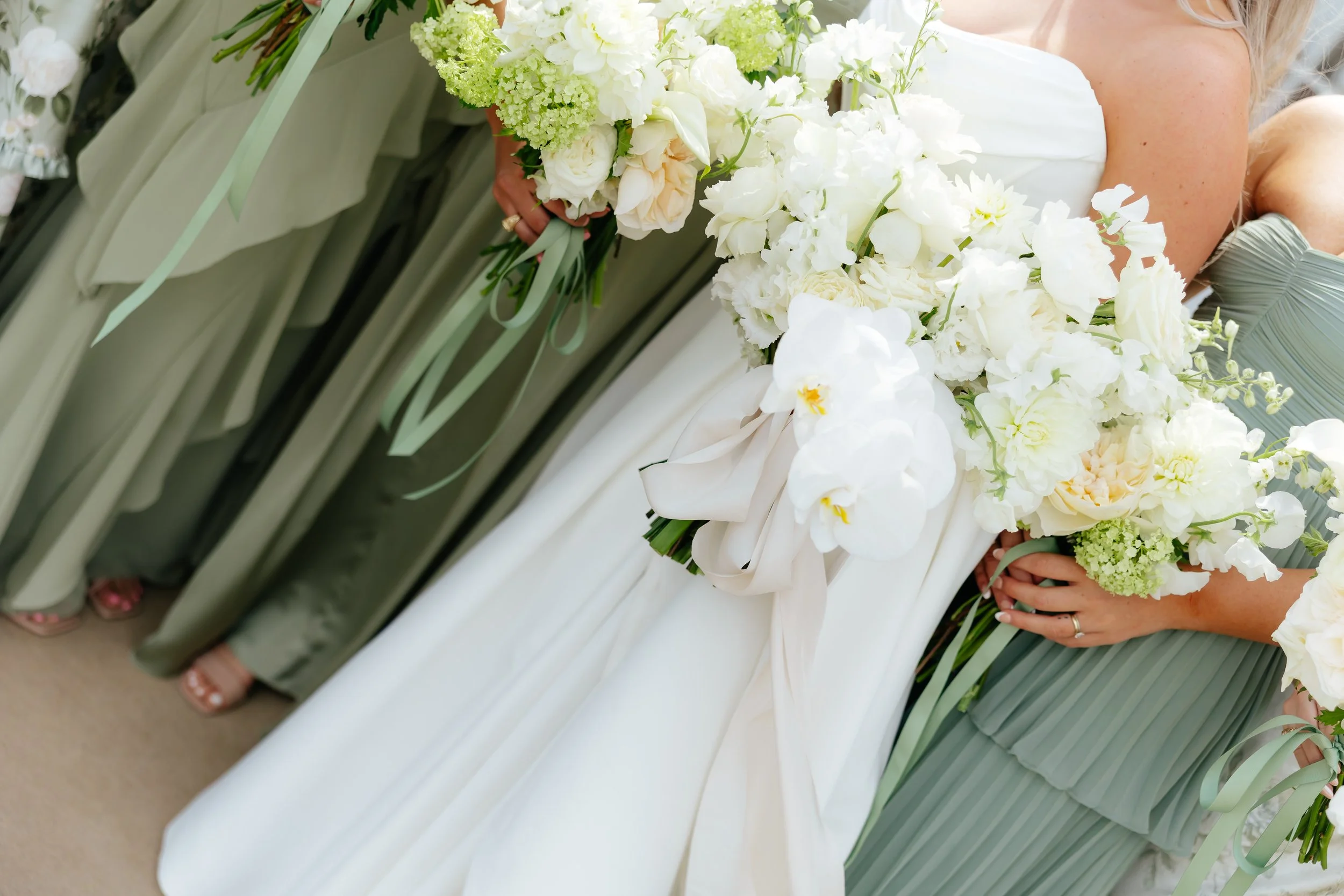 Bridesmaids and bride holding large floral bouquets with white and green flowers at a wedding.