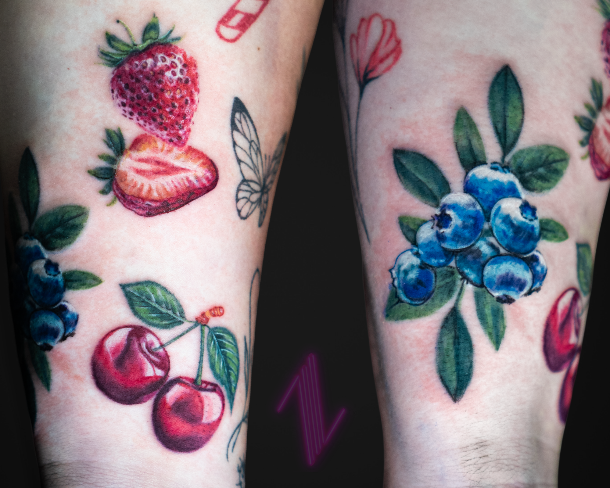 Close-up of colorful tattoos on skin featuring strawberries, cherries, blueberries, and floral elements.