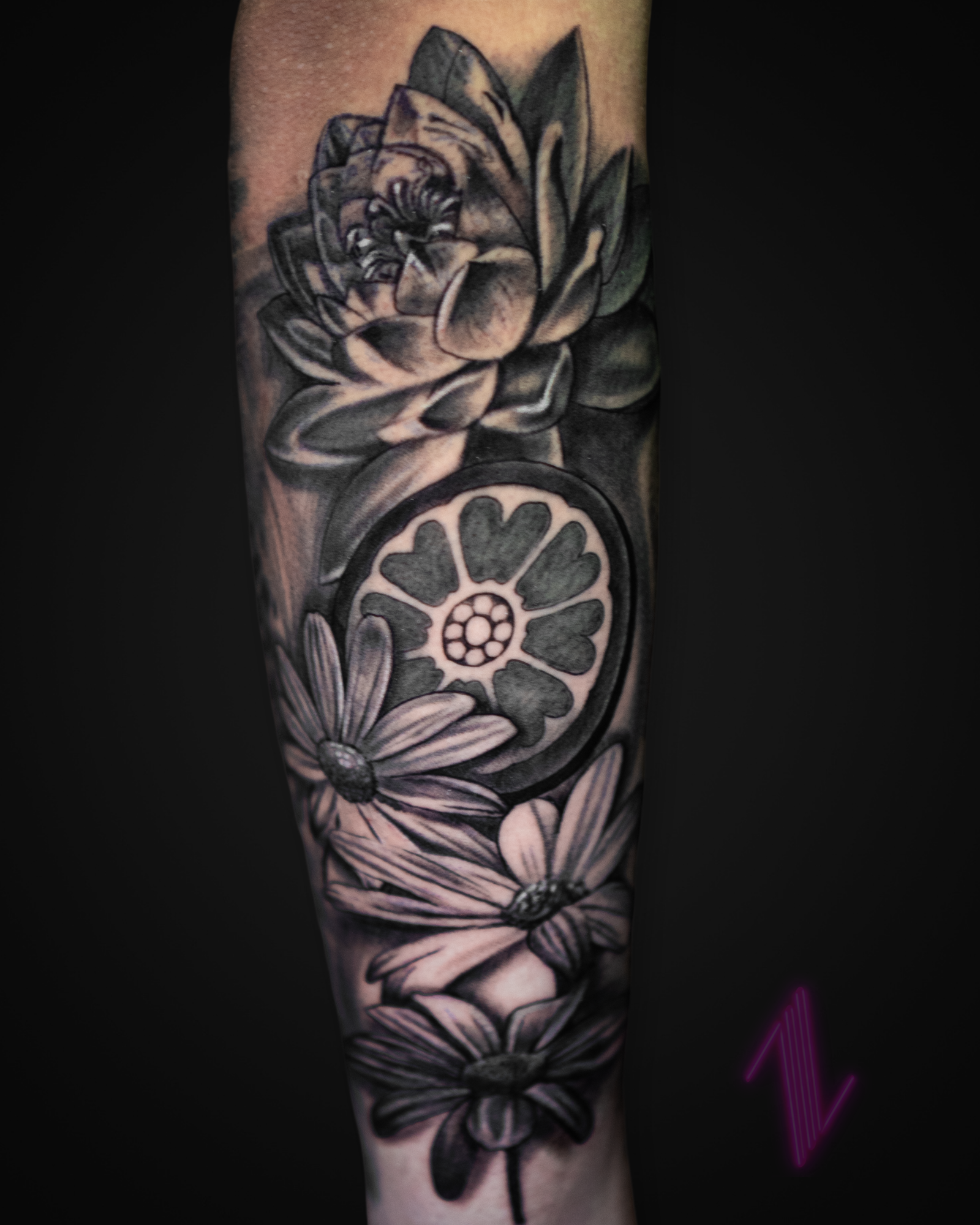 Black and gray tattoo of a dragonfly, daisies, and a large lotus flower on a person's arm.