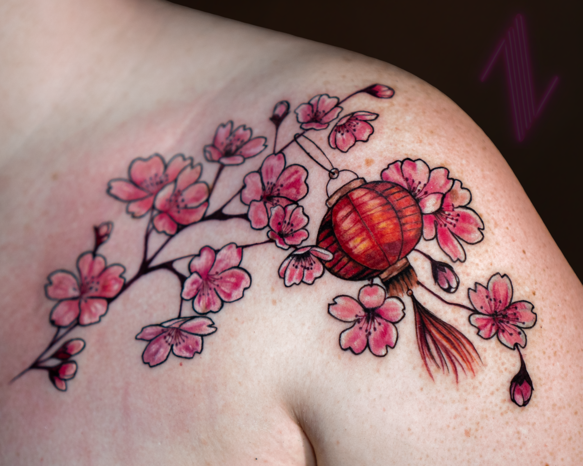 Tattoo of pink cherry blossoms surrounding a red paper lantern on a person's shoulder.