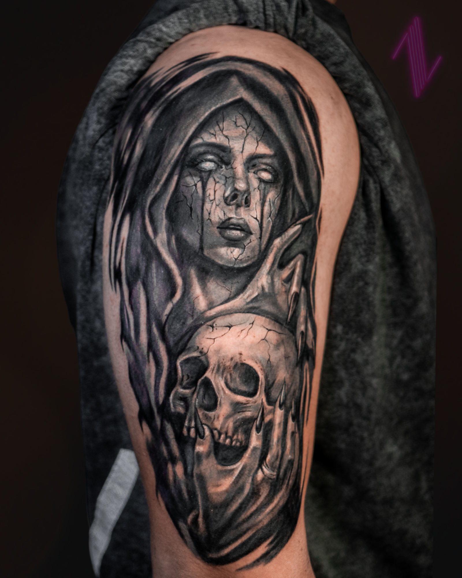 Black and gray tattoo of a woman's face with long hair, cracking scars, and pale eyes, holding a skull with cracked surface and dark eye sockets.