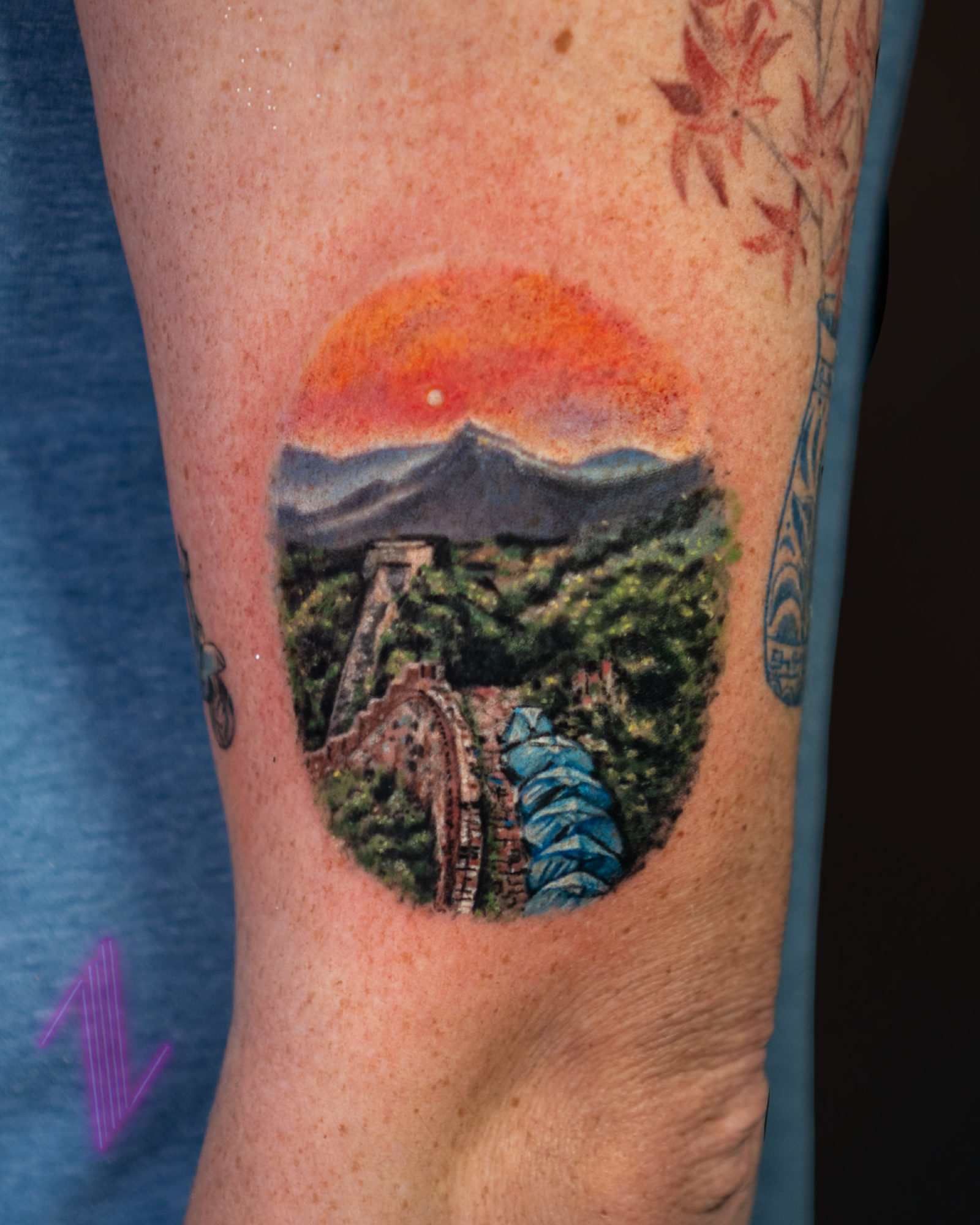 Tattoo of Mount Fuji with a sunset and a bridge over a river, surrounded by greenery.