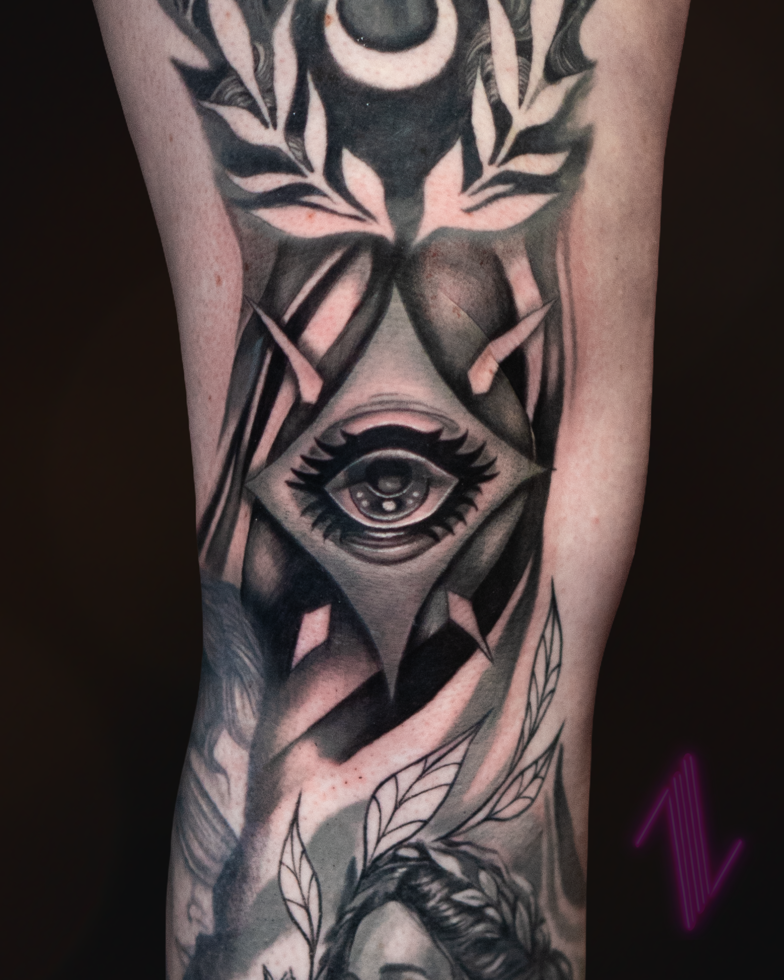 Tattoo of an eye within a diamond shape, with surrounding abstract and floral elements.