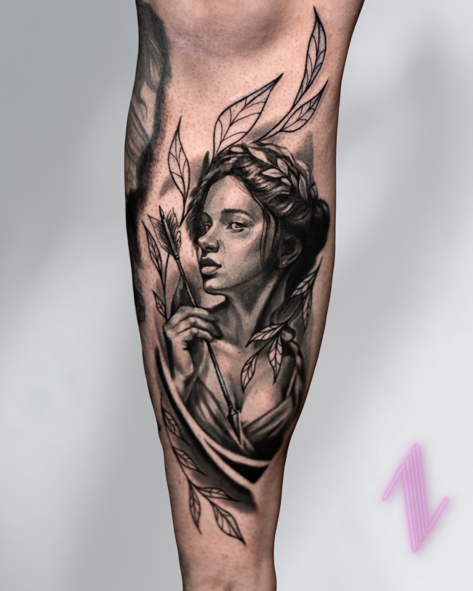 Tattoo of a woman's face with long hair, surrounded by leaves, on a person's arm.