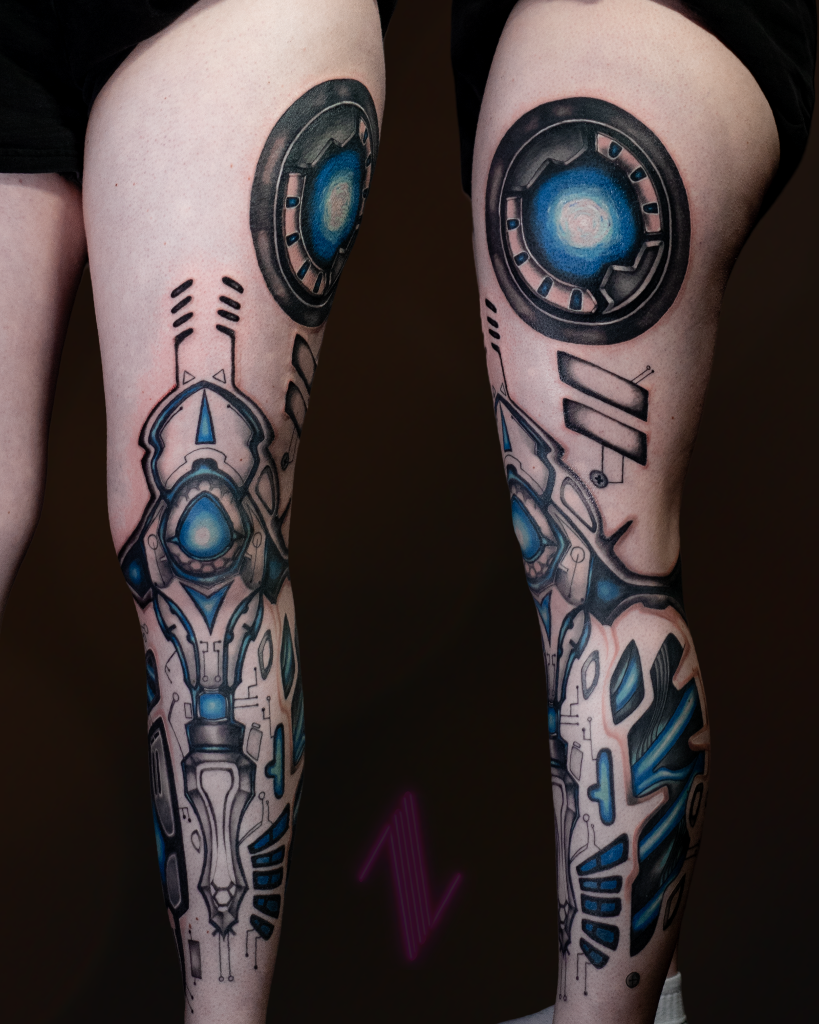 Tattooed legs with symmetrical sci-fi and robotic designs in blue and black ink.