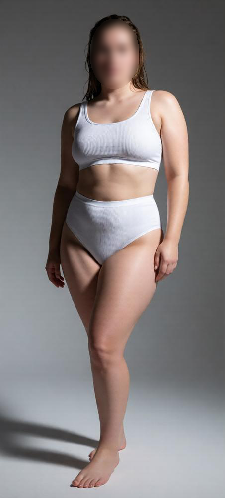 A woman standing in a studio setting wearing a white tank top and high-waisted underwear, with a gray background.