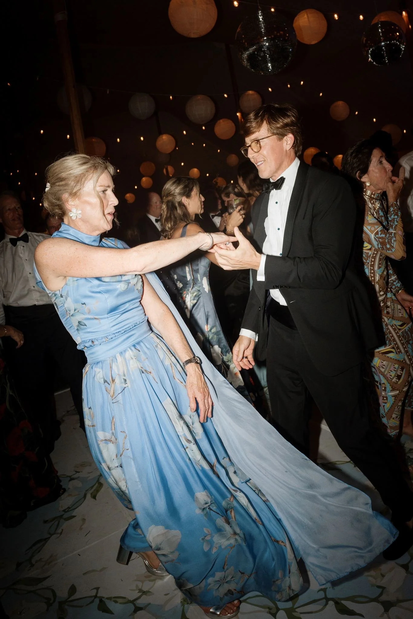 Joanelle Cannell dancing at a black-tie wedding in a flowing blue floral mother of the bride gown by Gramercy Atelier.