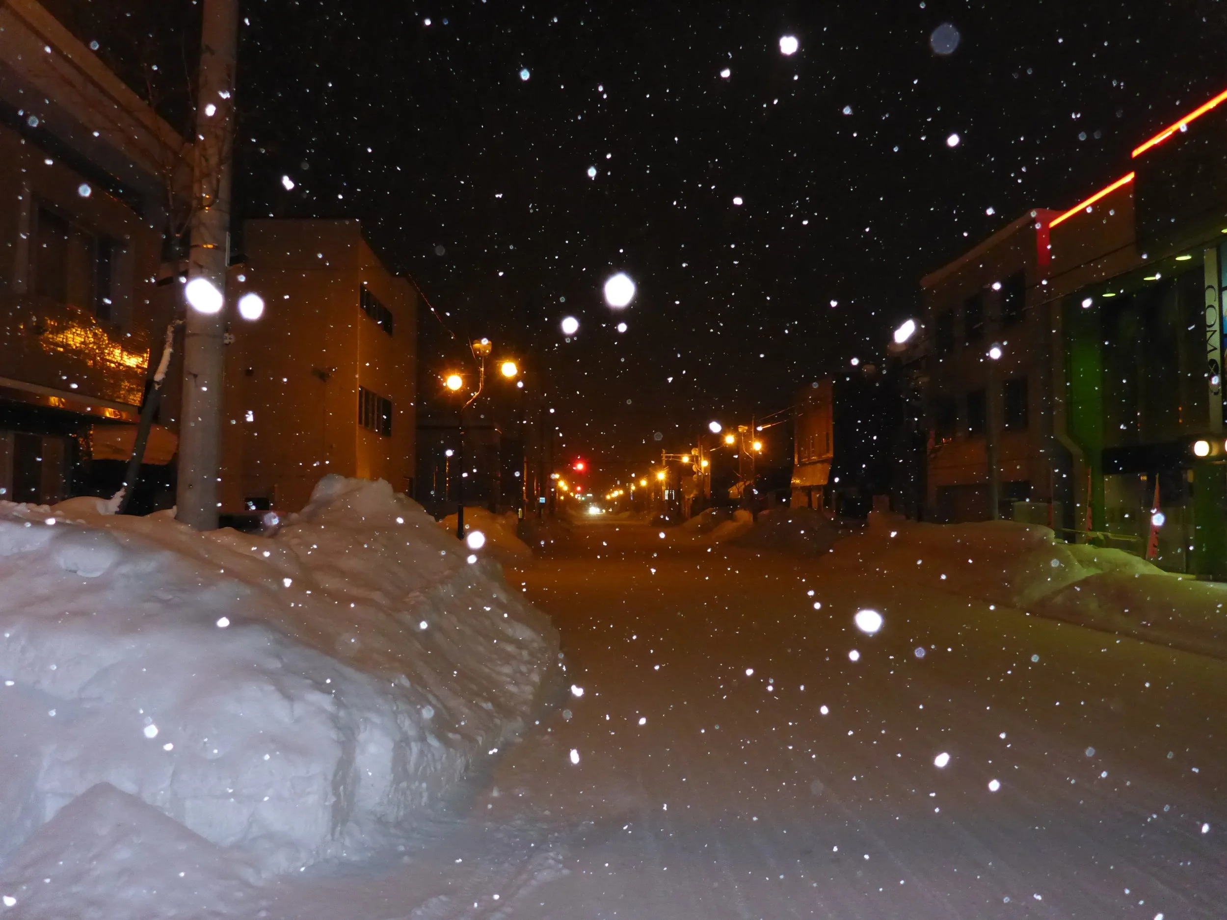 Snowy street at night with falling snowflakes and streetlights illuminating the scene in Hokkaido Japan.