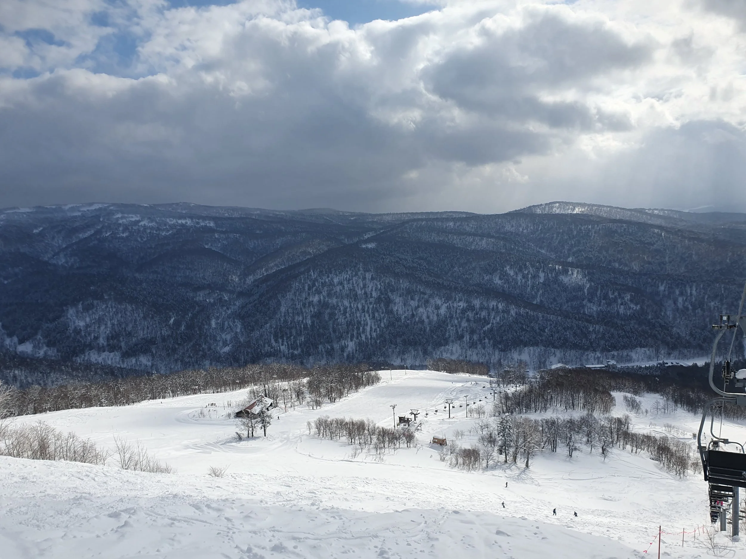 Snow-covered ski resort with mountainous landscape, ski lift, and trees in Hokkaido Japan.