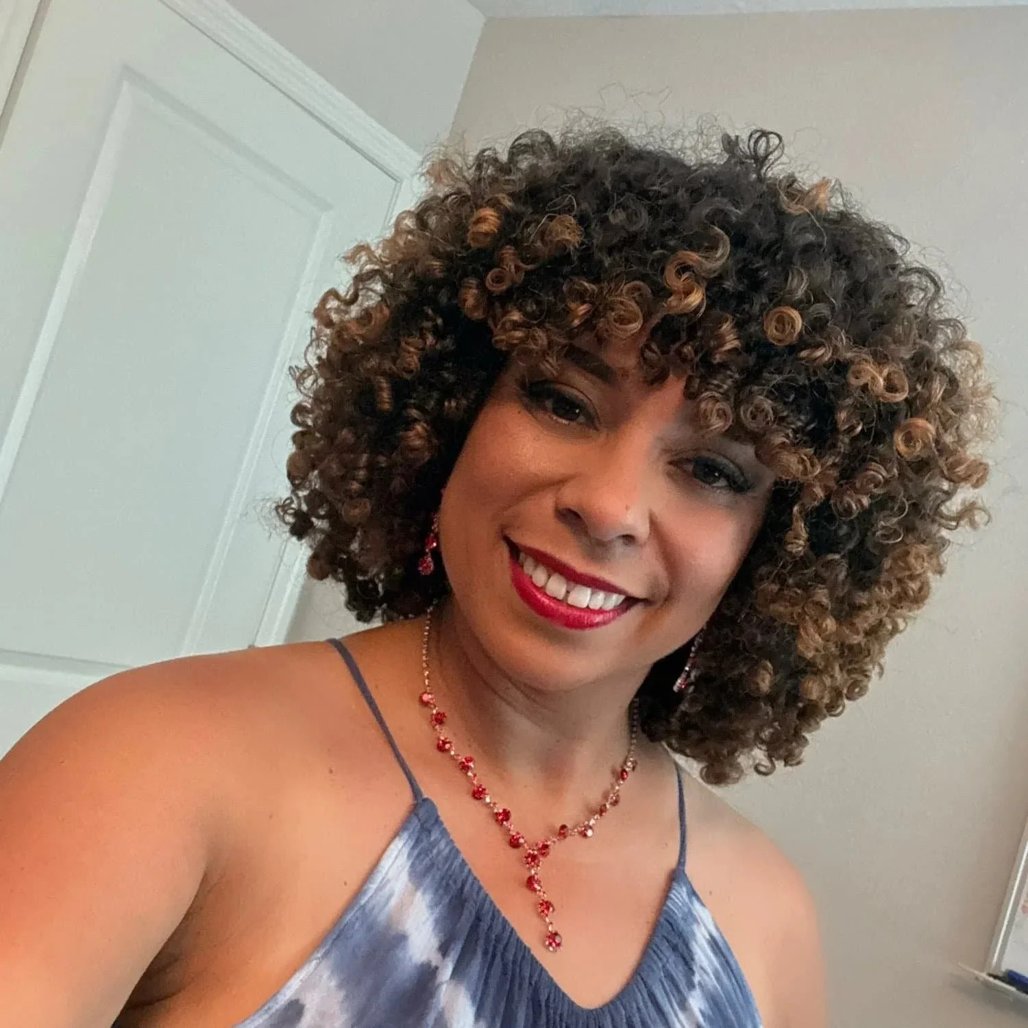 Modern house with wooden exterior embedded in a mountainous landscape, with a large glass window reflecting two people inside, surrounded by yellow plants and green shrubs.