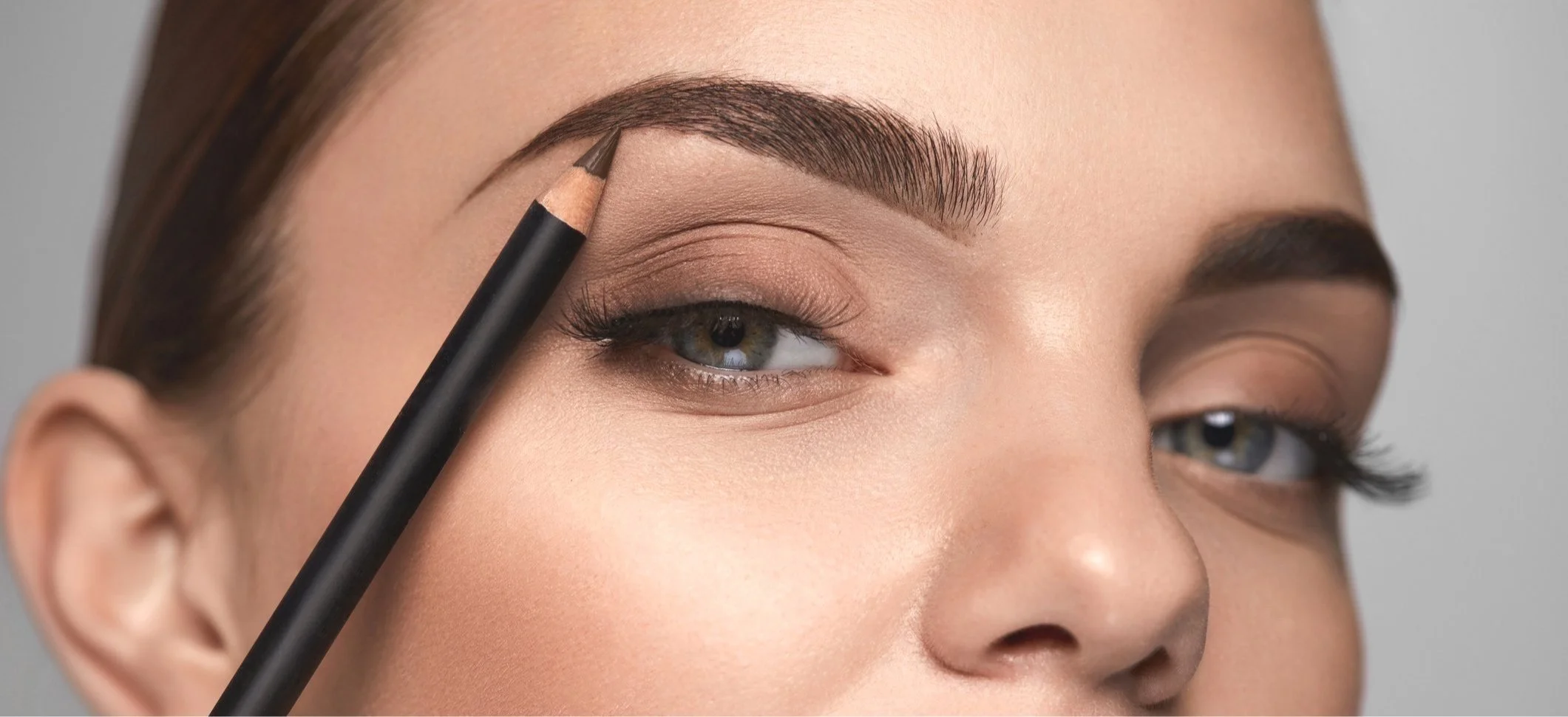 A woman with well-groomed eyebrows is filling in her eyebrows with a pencil.