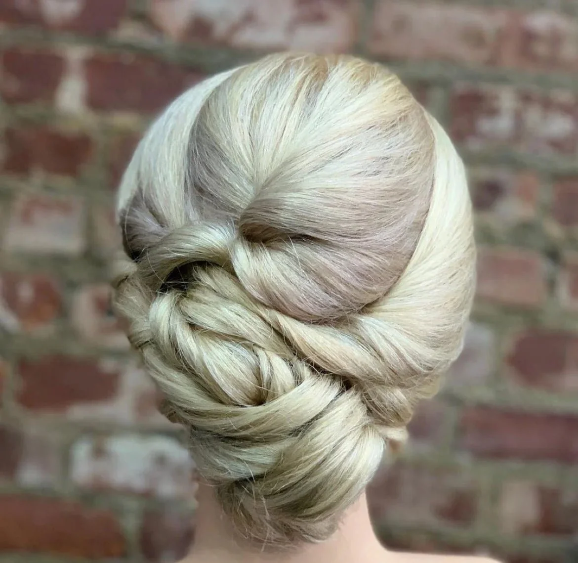 Blonde hair styled in an elegant twisted updo with a brick wall background Curly hair specialist Tampa