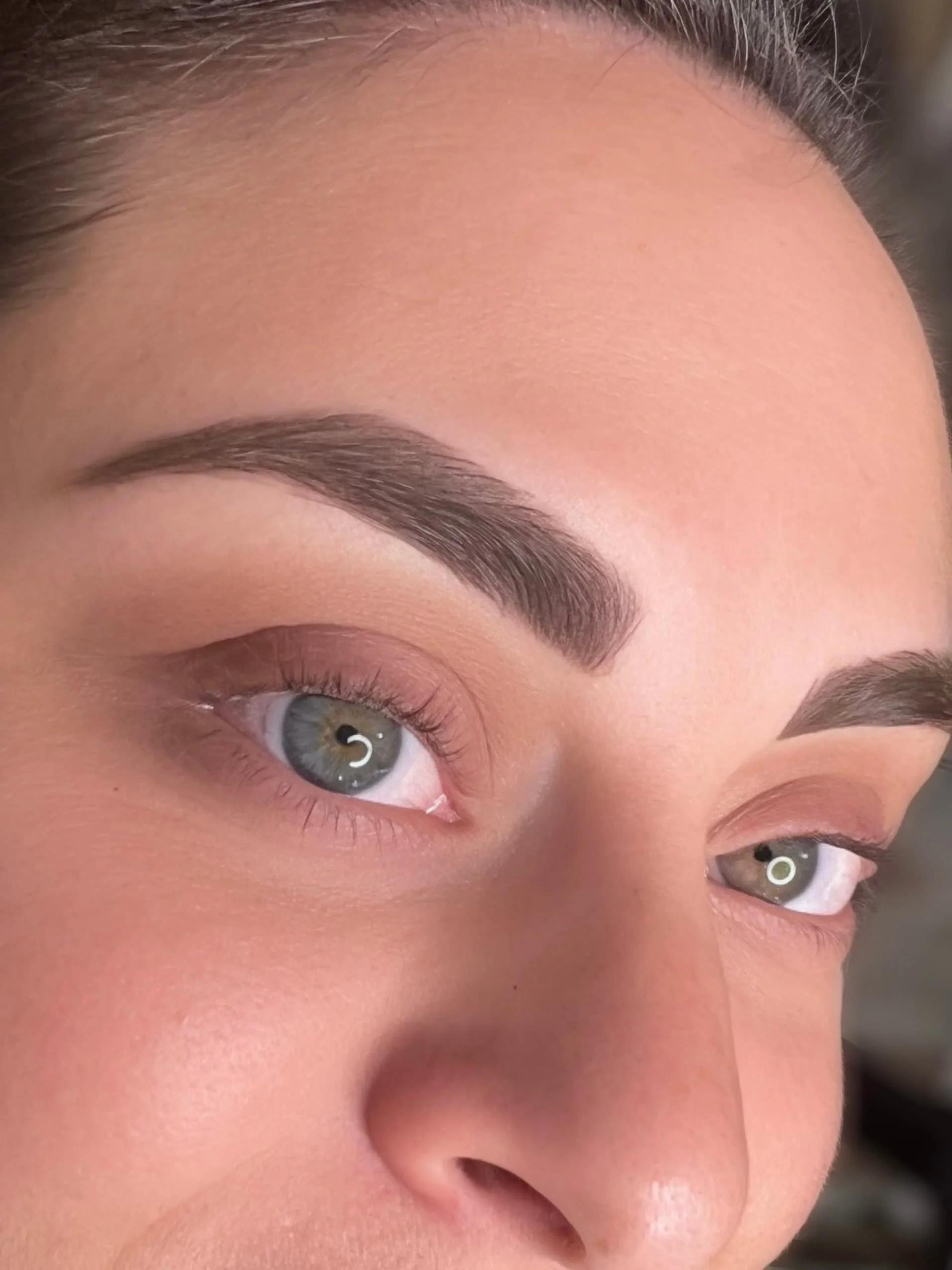Close-up of a woman with well-groomed eyebrows, eye makeup, and gray eyes.