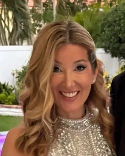 Woman with blonde curly hair smiling, wearing a sparkly dress outdoors.