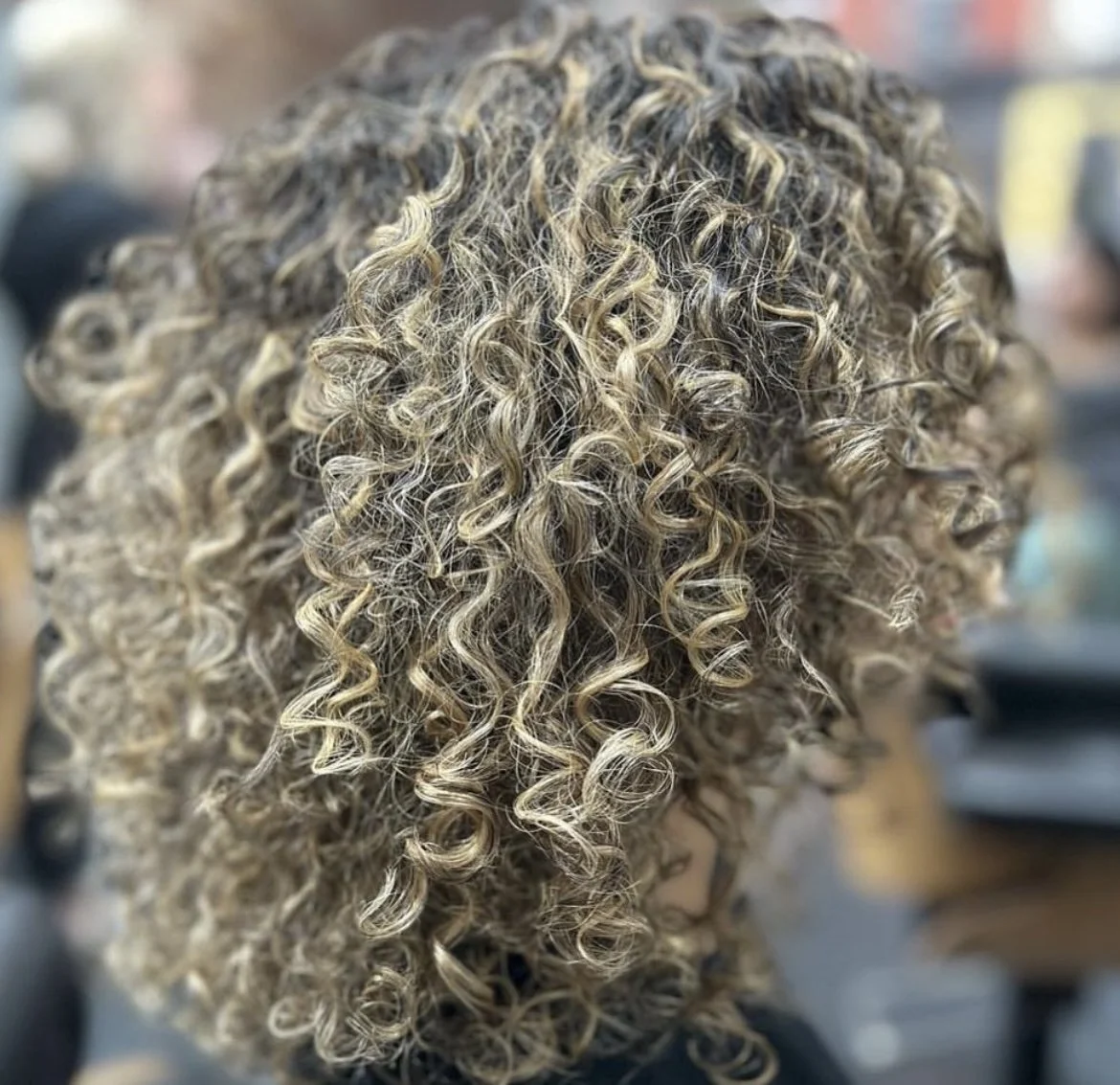 Close-up of a person's curly blonde hair with highlights.