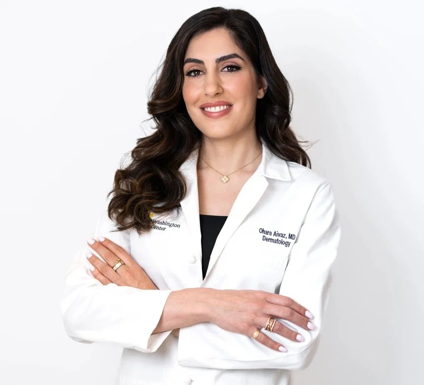Dr. Ohara Aivaz, double board-certified dermatologist, standing in a white lab coat with arms crossed against a white background.