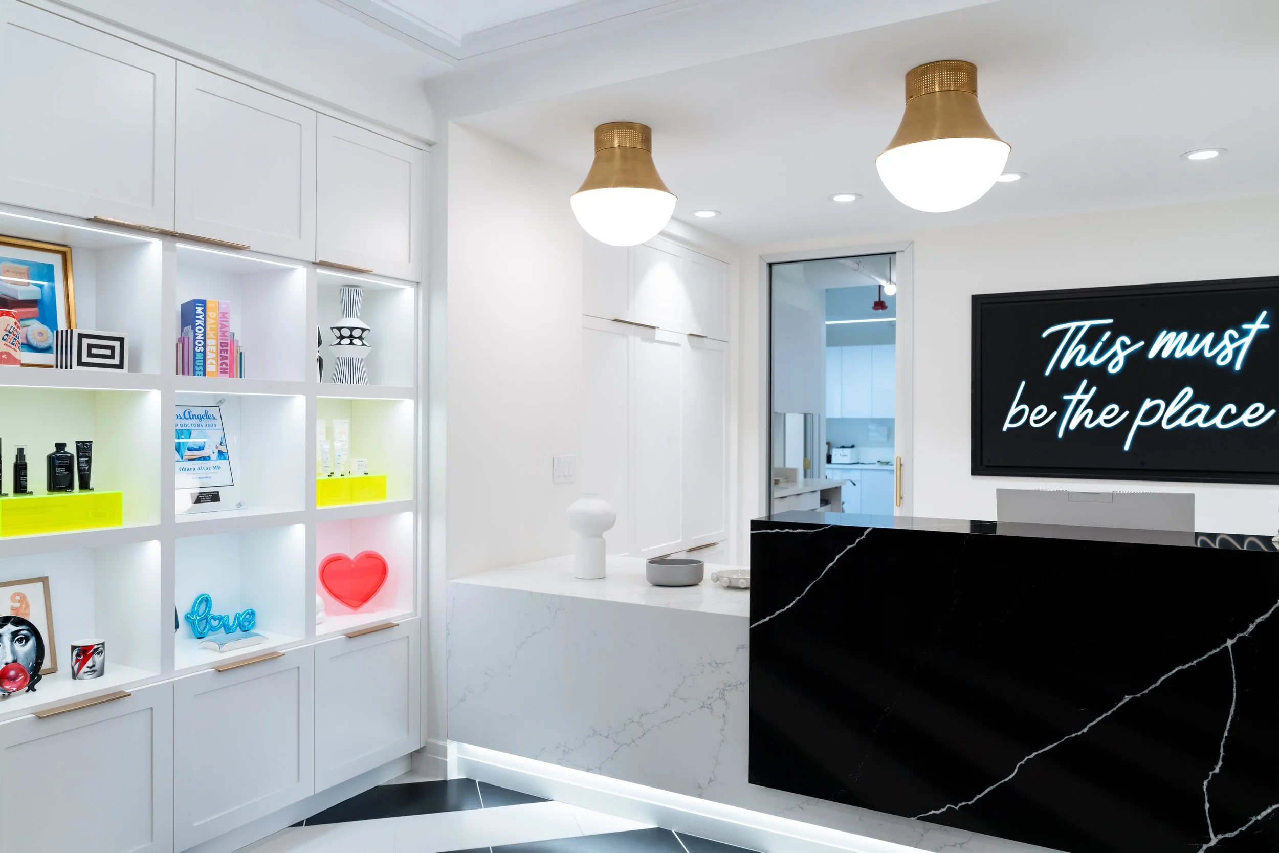 Modern reception area at Ohara Dermatology office featuring white shelving, decorative accents, marble front desk, and contemporary lighting.