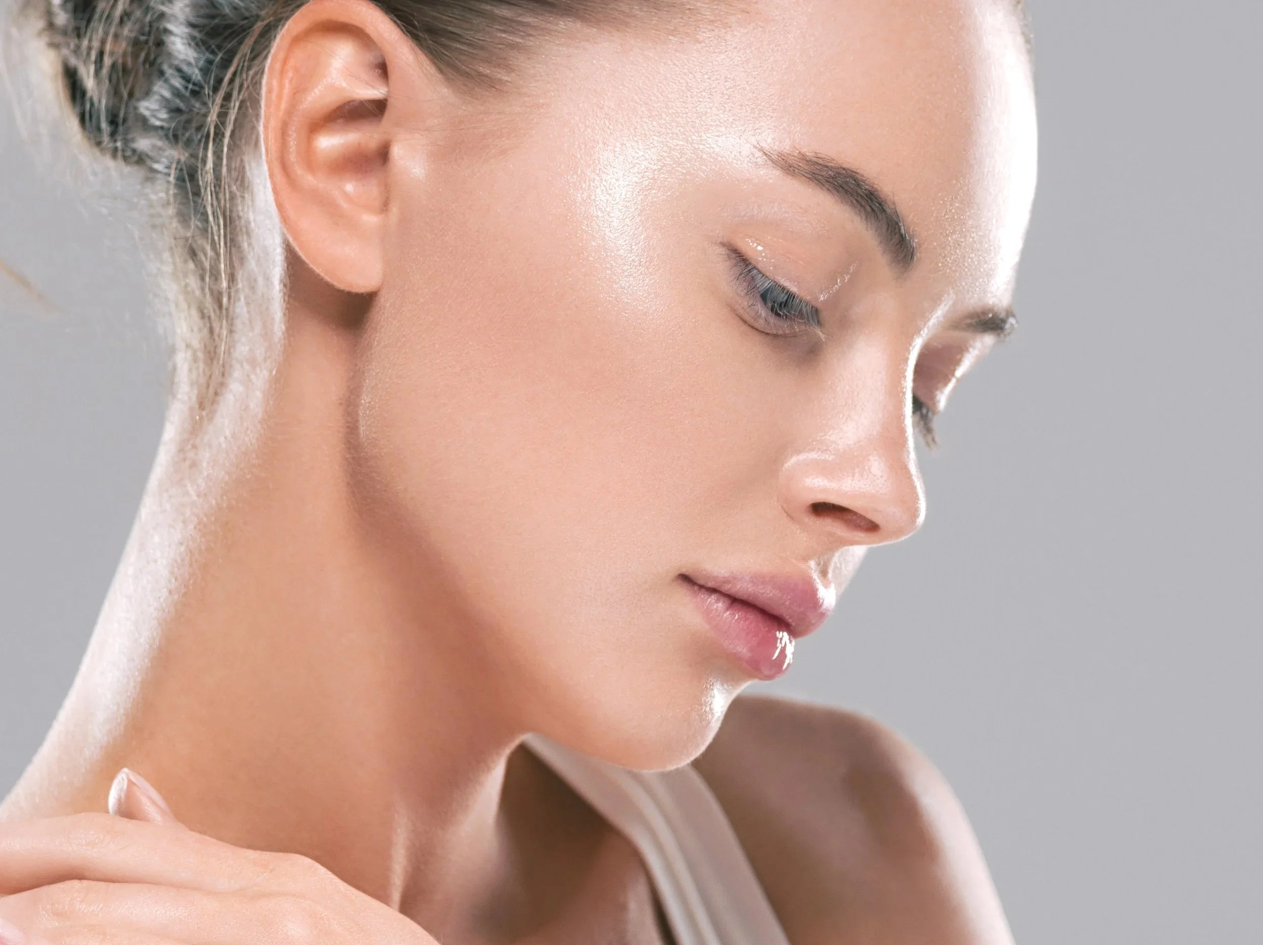 Close-up of a woman's face with clear, glowing skin, her eyes closed, and her hand gently touching her shoulder.