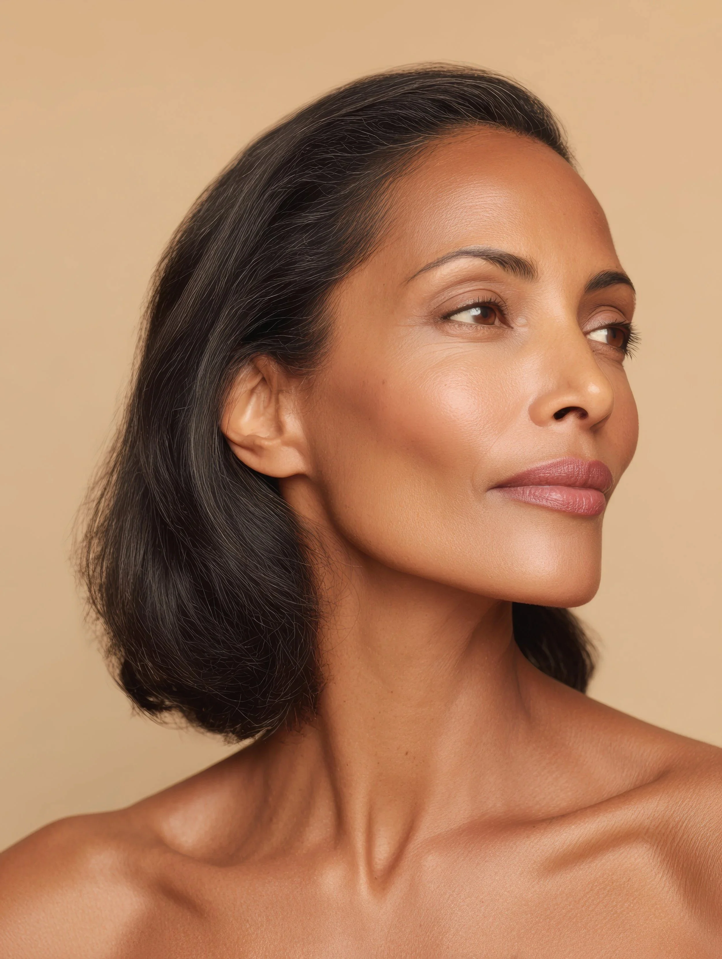 Close-up of a woman's face with smooth skin, dark hair, and a calm expression against a beige background.