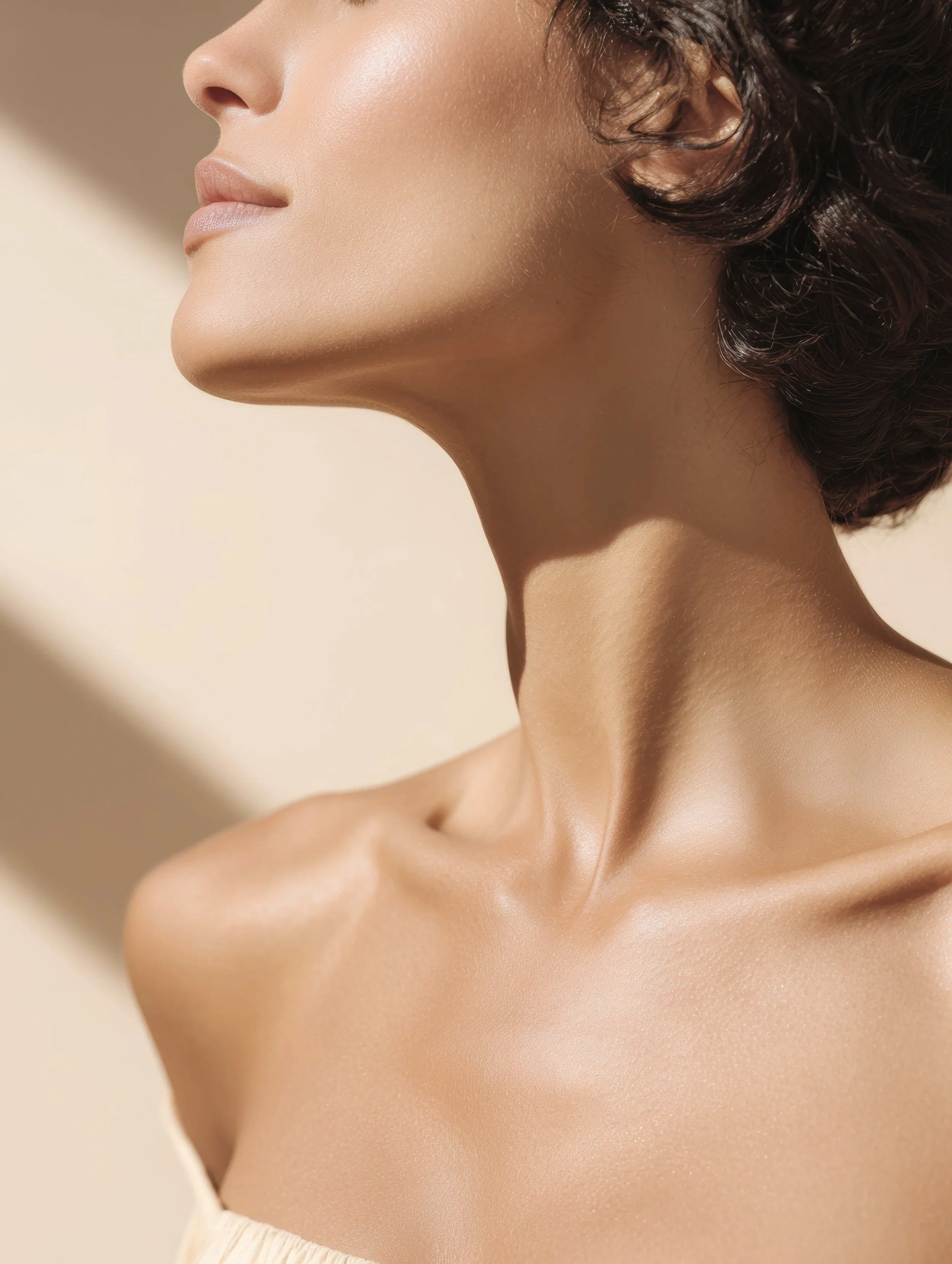 Close-up of a woman's smooth neck, shoulder, and face, with her head tilted slightly back, showing a side profile in natural light.